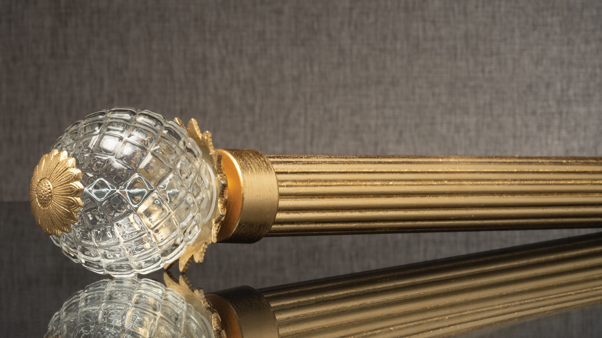 Decorative crystal and gold-topped baton lying on a reflective surface with a gray background