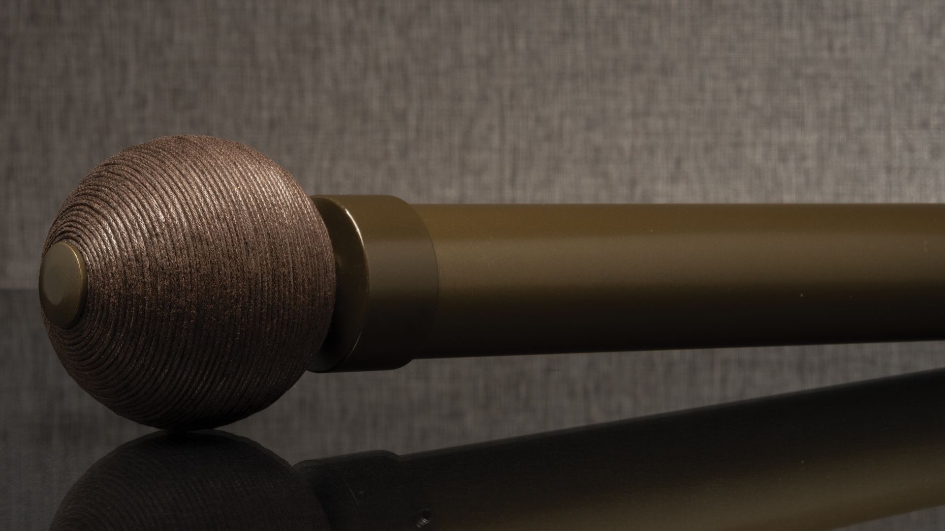 Close-up of a handheld microphone with a silver mesh head and dark handle on a reflective surface