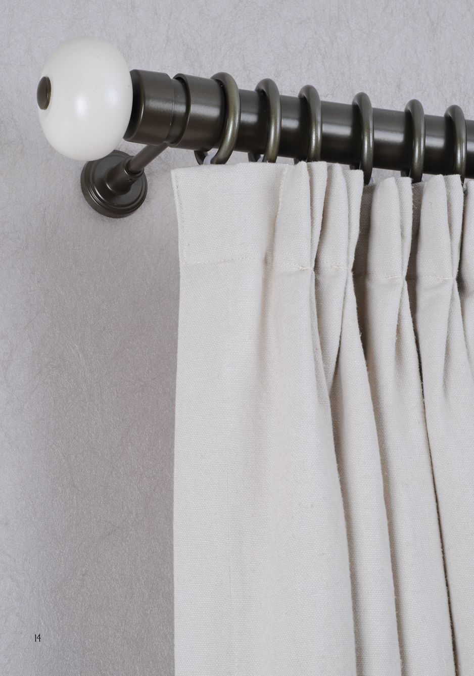 White curtains on a black curtain rod with a white finial against a gray wall