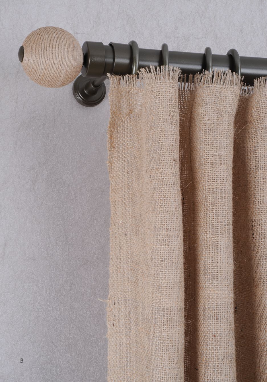Burlap curtains hang from a black curtain rod with a round woven finial.