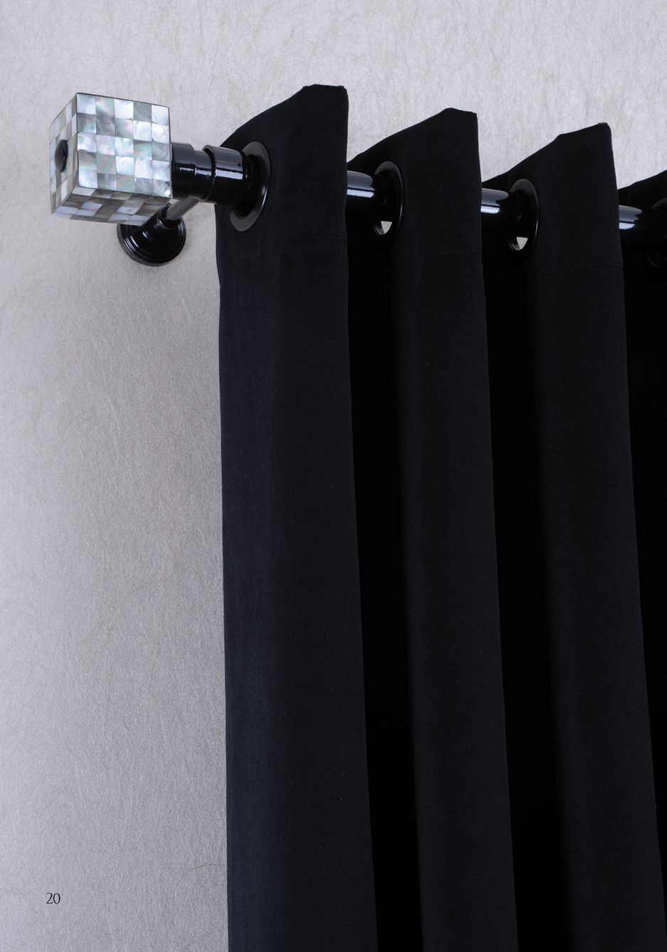 Black curtain panel on a silver rod with a clear decorative finial against a light wall.