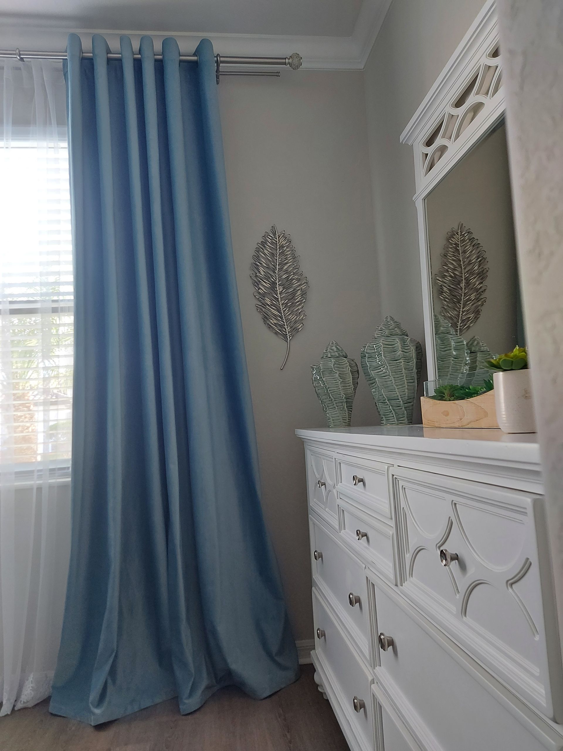 Light blue curtains beside a white dresser with mirror in a bright bedroom corner