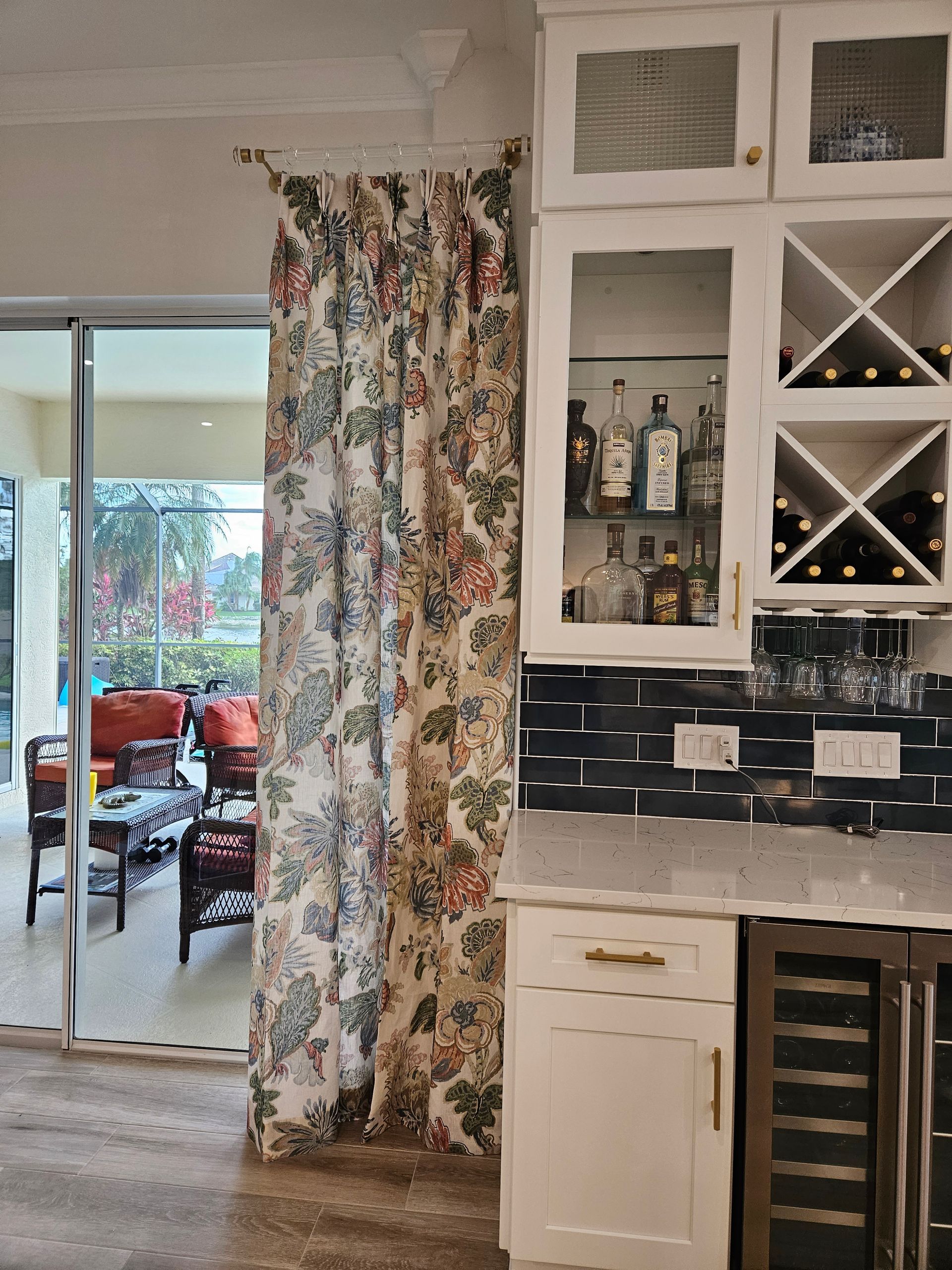 Kitchen with white cabinets, black tile backsplash, wine rack, and a floral curtain by sliding glass doors.