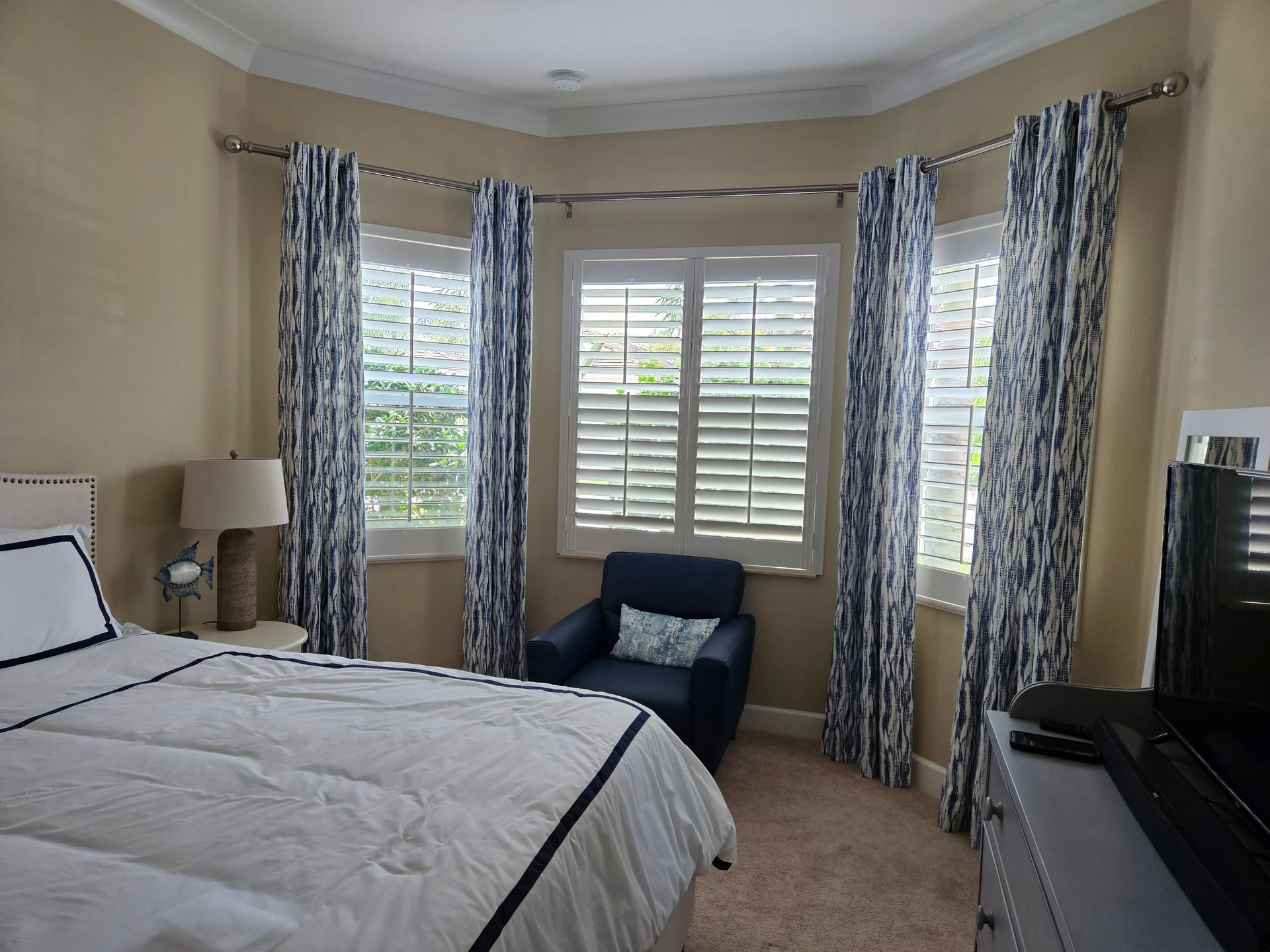 Bedroom with a bed, armchair, bay window with shutters, and floral curtains