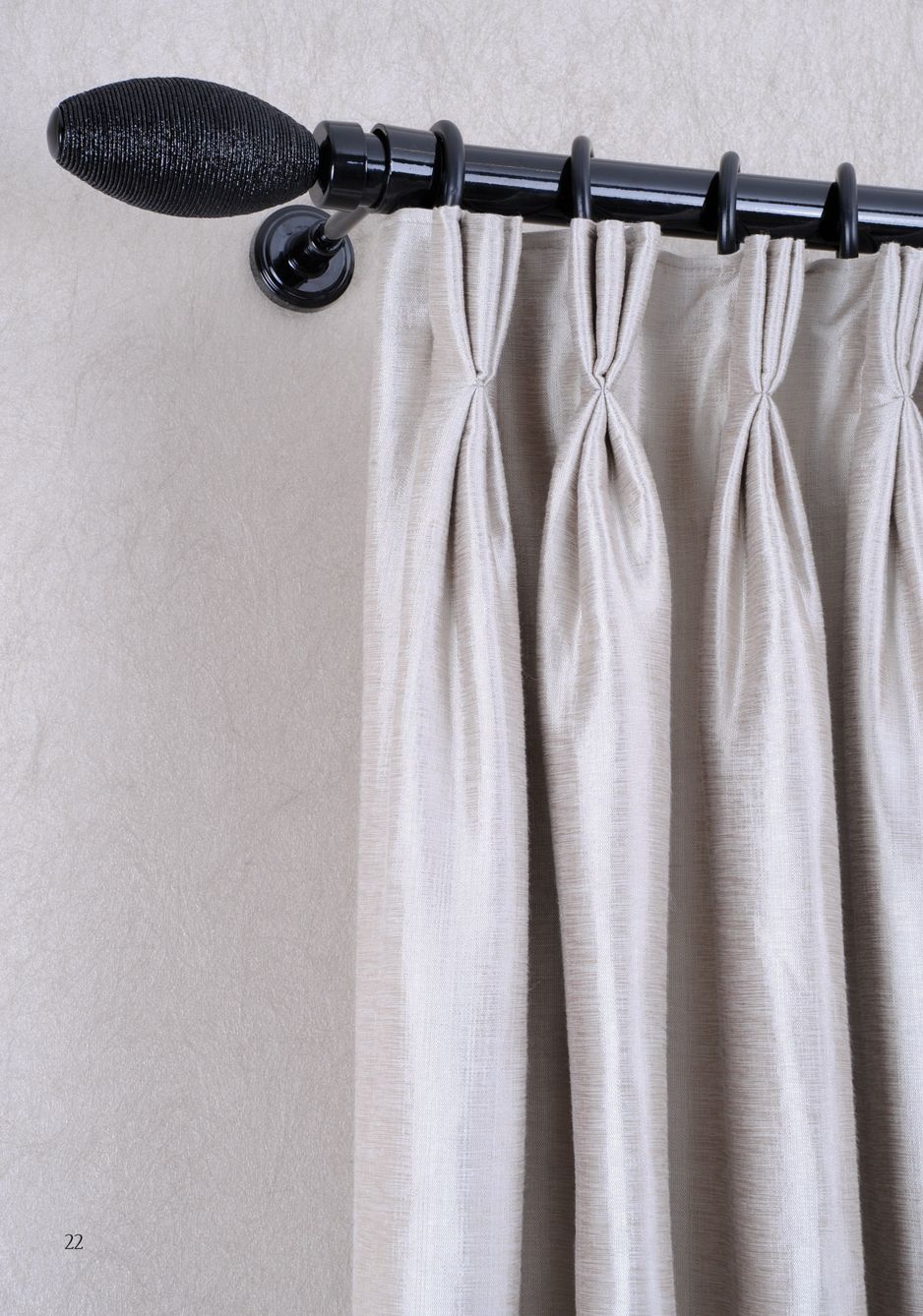 Black curtain rod with leaf finial holding cream curtains against a gray wall