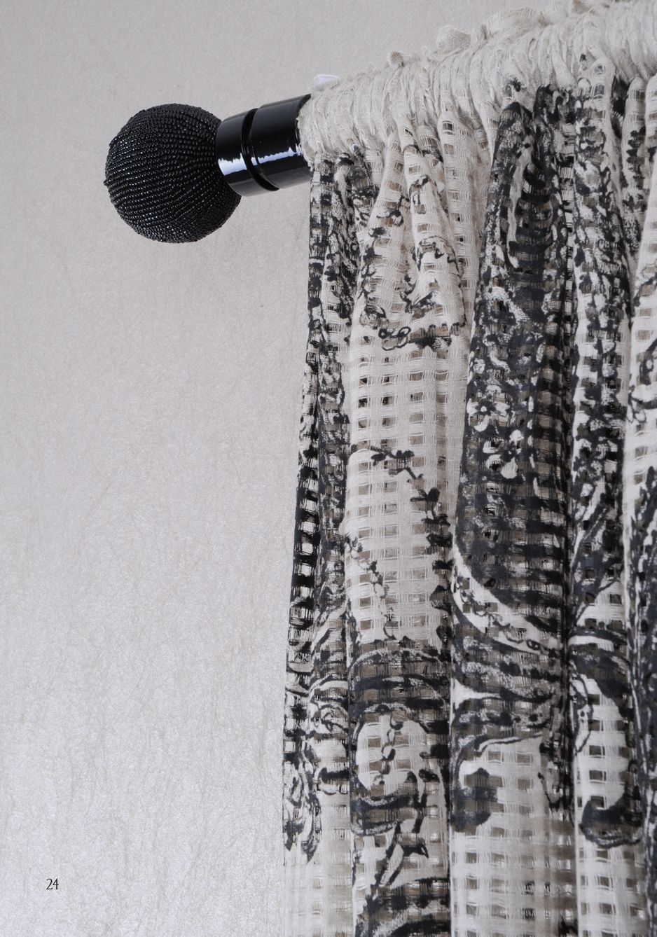 Black curtain rod with sheer patterned curtains against a light wall
