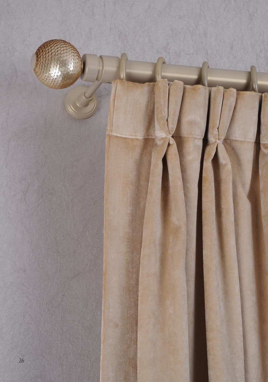 Beige curtain on a metal rod with a decorative gold finial against a gray wall