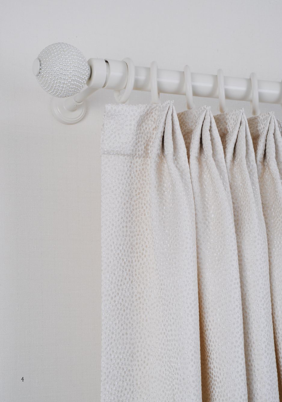 White curtains hanging on a white curtain rod with a clear decorative finial against a white wall