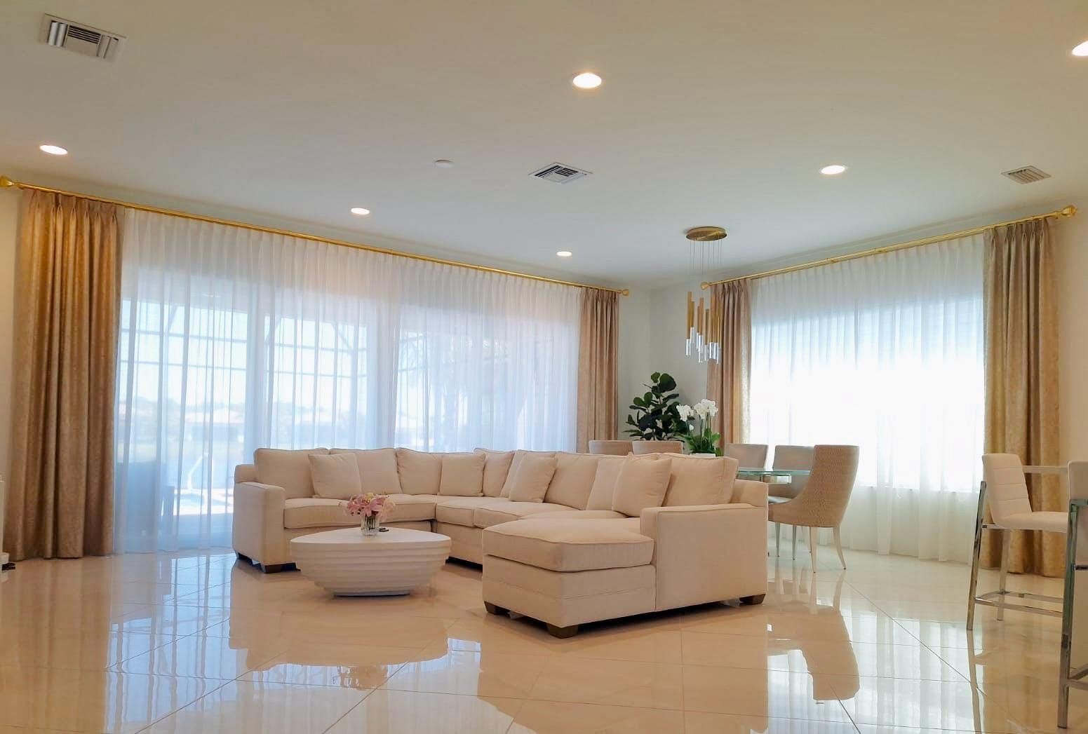 Bright modern living room with cream sectional sofa, large windows, sheer curtains, and glossy tiled floor
