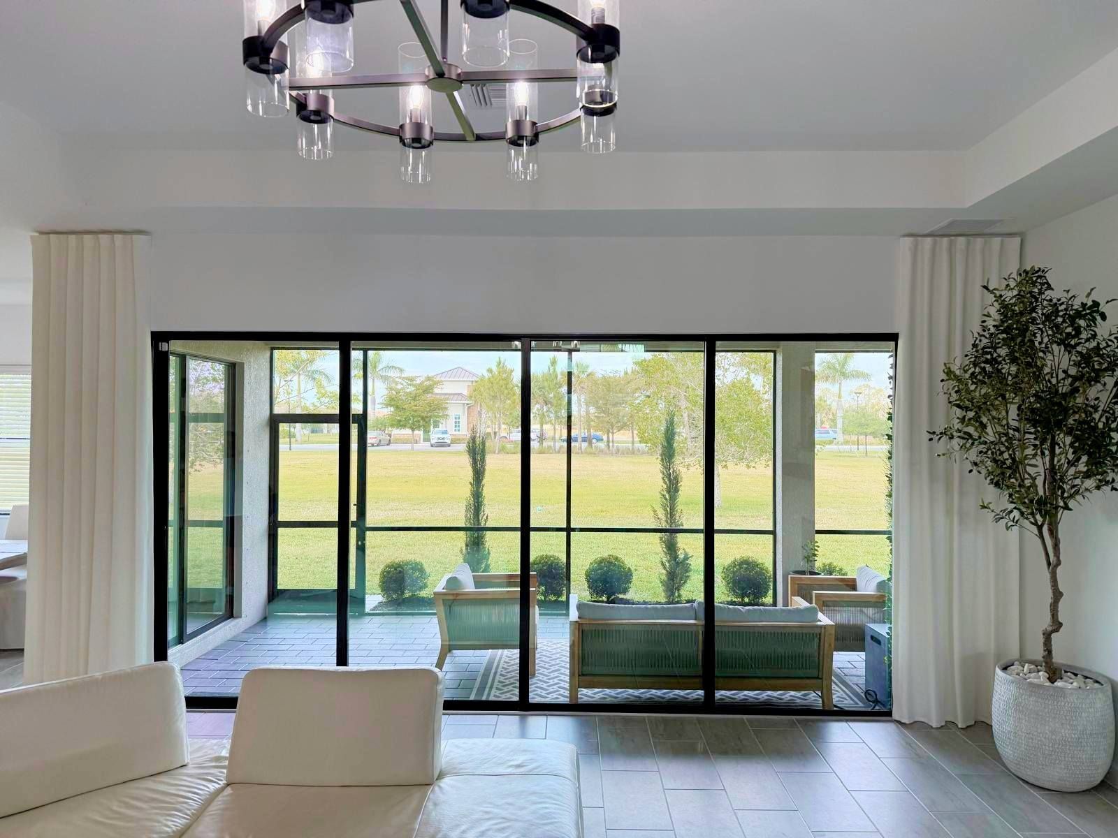 Modern living room with floor-to-ceiling glass doors, white furniture, and a view of a green yard