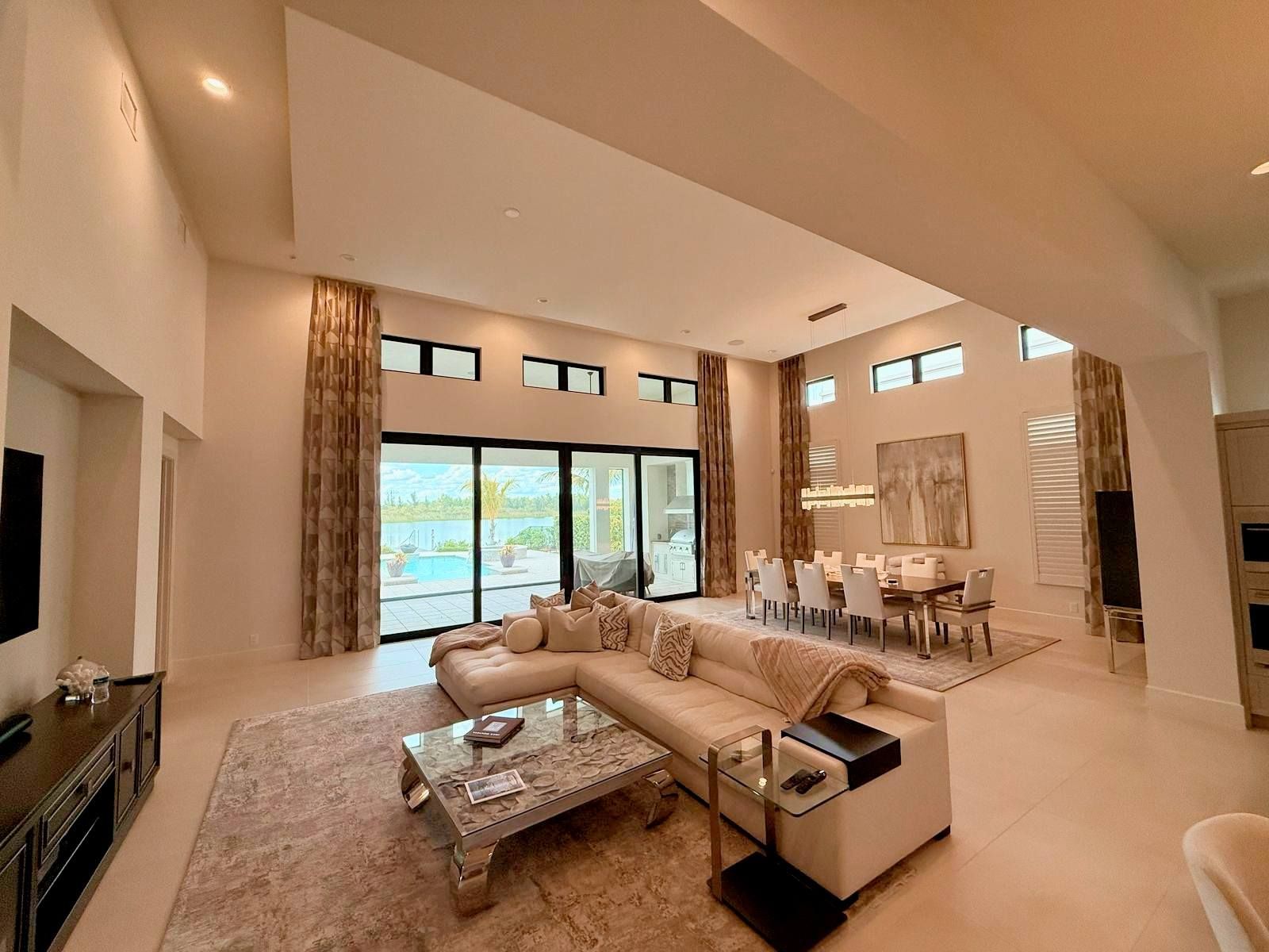 Spacious modern living room with beige sectional, coffee table, fireplace, and large windows overlooking a pool.
