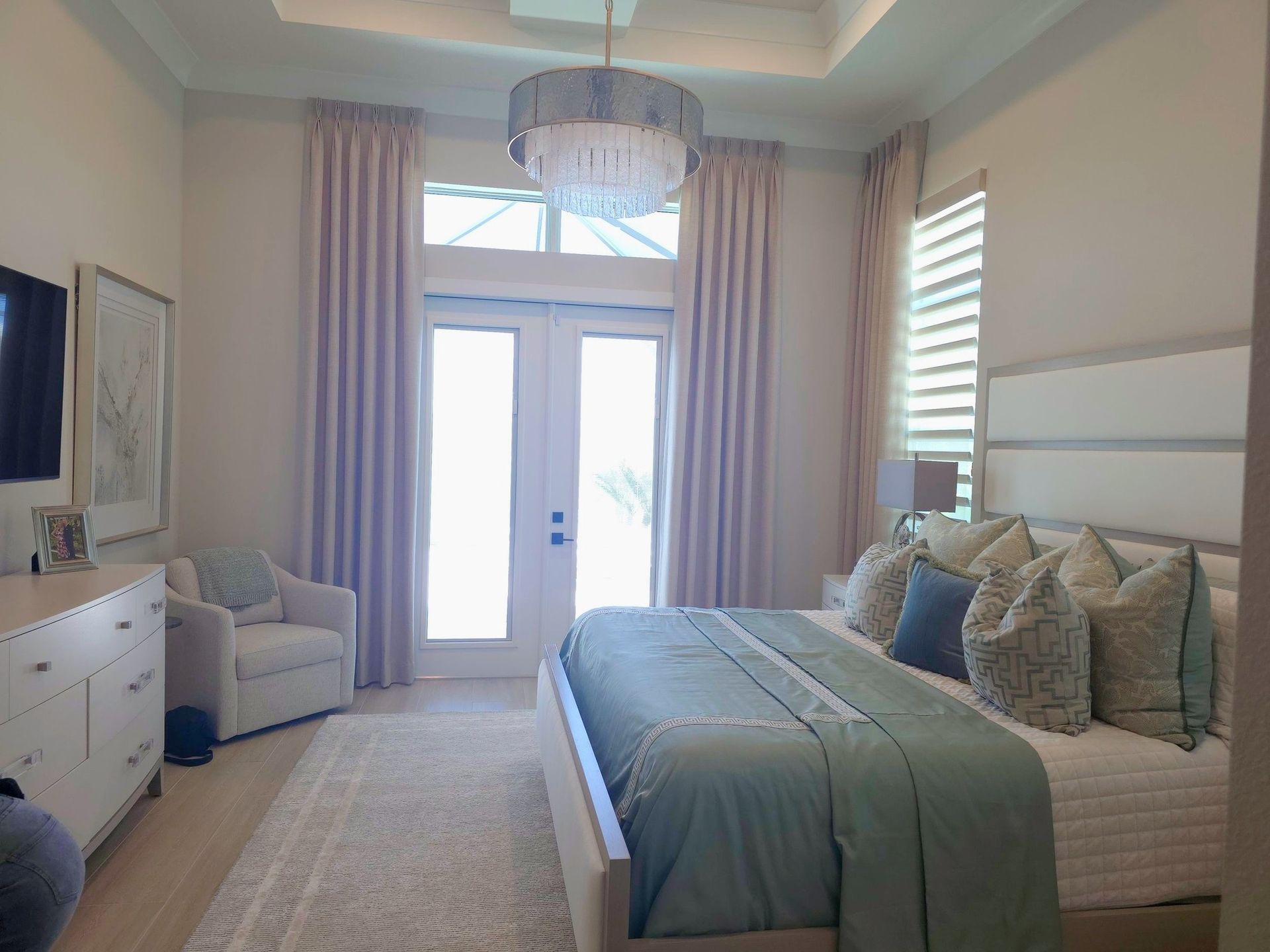 Bright bedroom with a large bed, dresser, mirror, and French doors to a balcony.