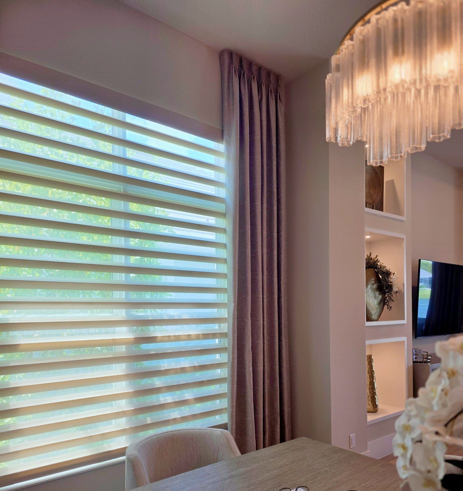 Bright dining nook with striped window shades, mauve curtains, and a crystal chandelier.