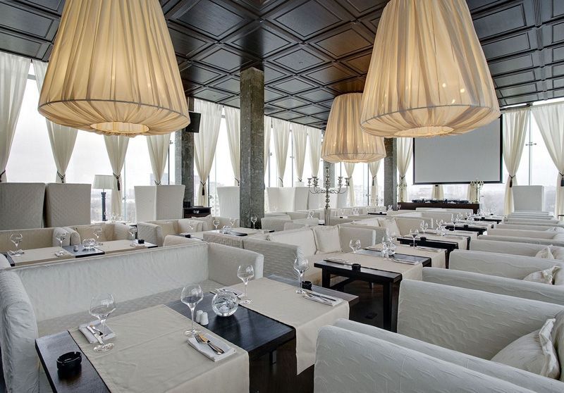 Bright modern restaurant with white lounge seating, dark tables, and large woven pendant lights