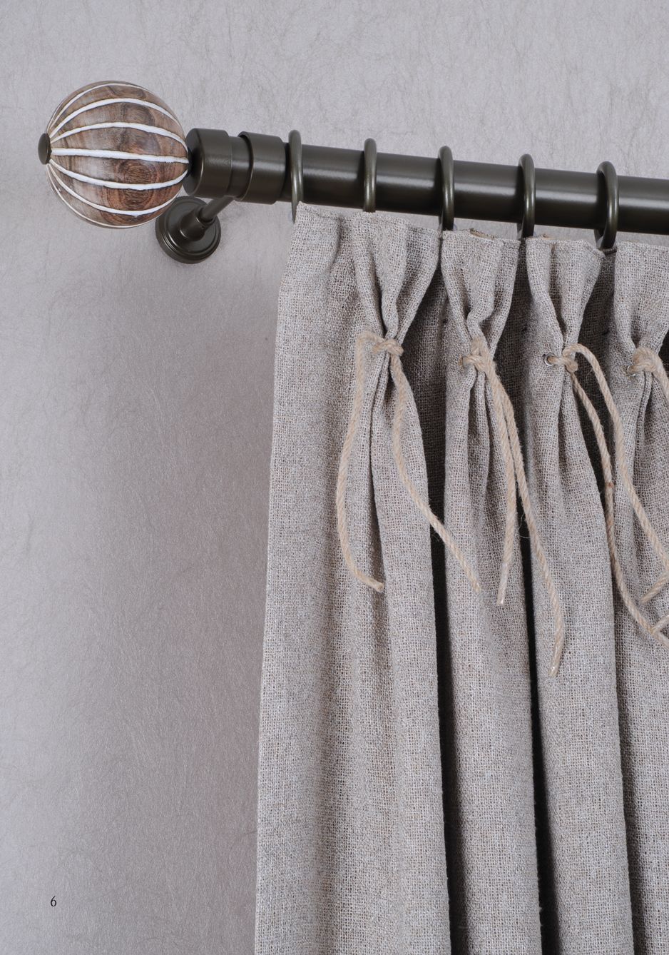 Black curtain rod with gray draped curtains and a decorative metal finial against a gray wall