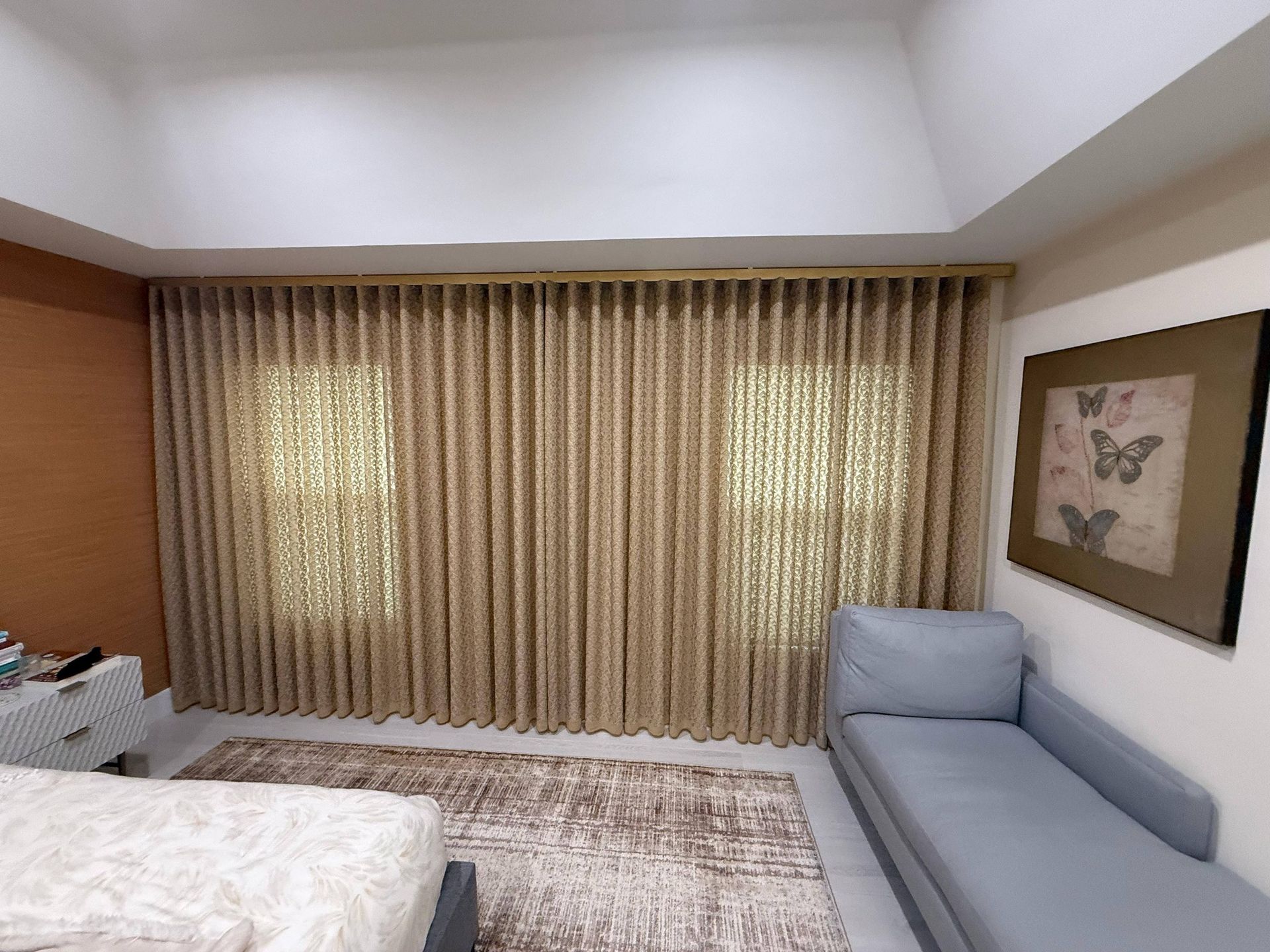 Bedroom with beige curtains, light gray sofa, framed wall art, and a bed with white bedding.