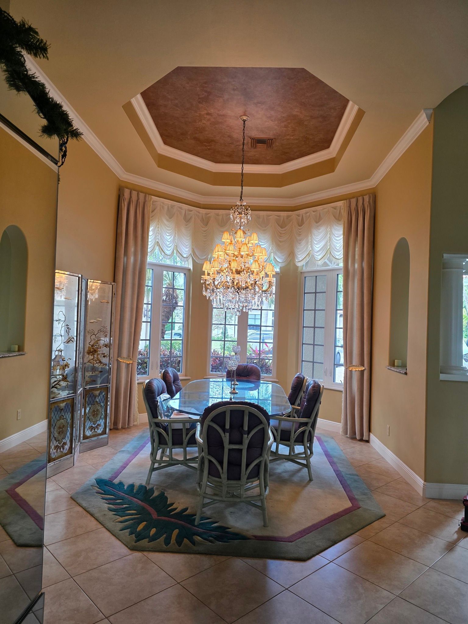 Elegant dining room with chandelier, glass table, and large windows with curtains.