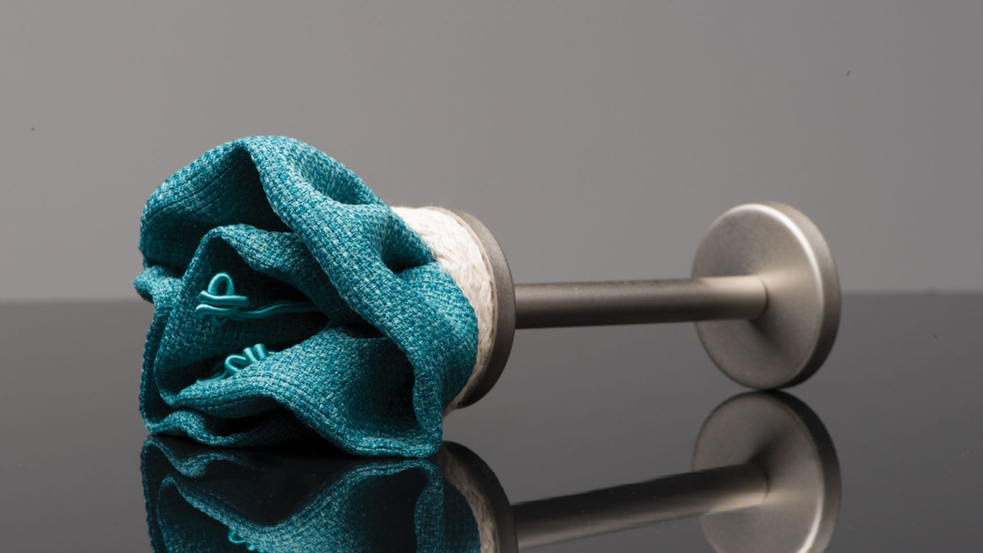 Teal cleaning cloth wrapped around a dumbbell on a reflective black surface