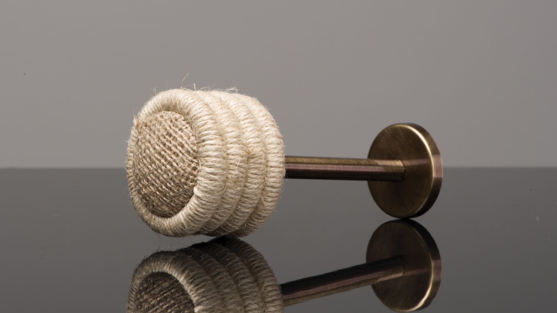 Beige braided rope on a bronze doorstop, resting on a glossy black surface with a reflection.