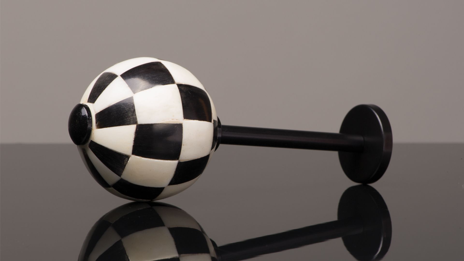 Black-and-white checkered dumbbell with spherical ends on a glossy reflective surface