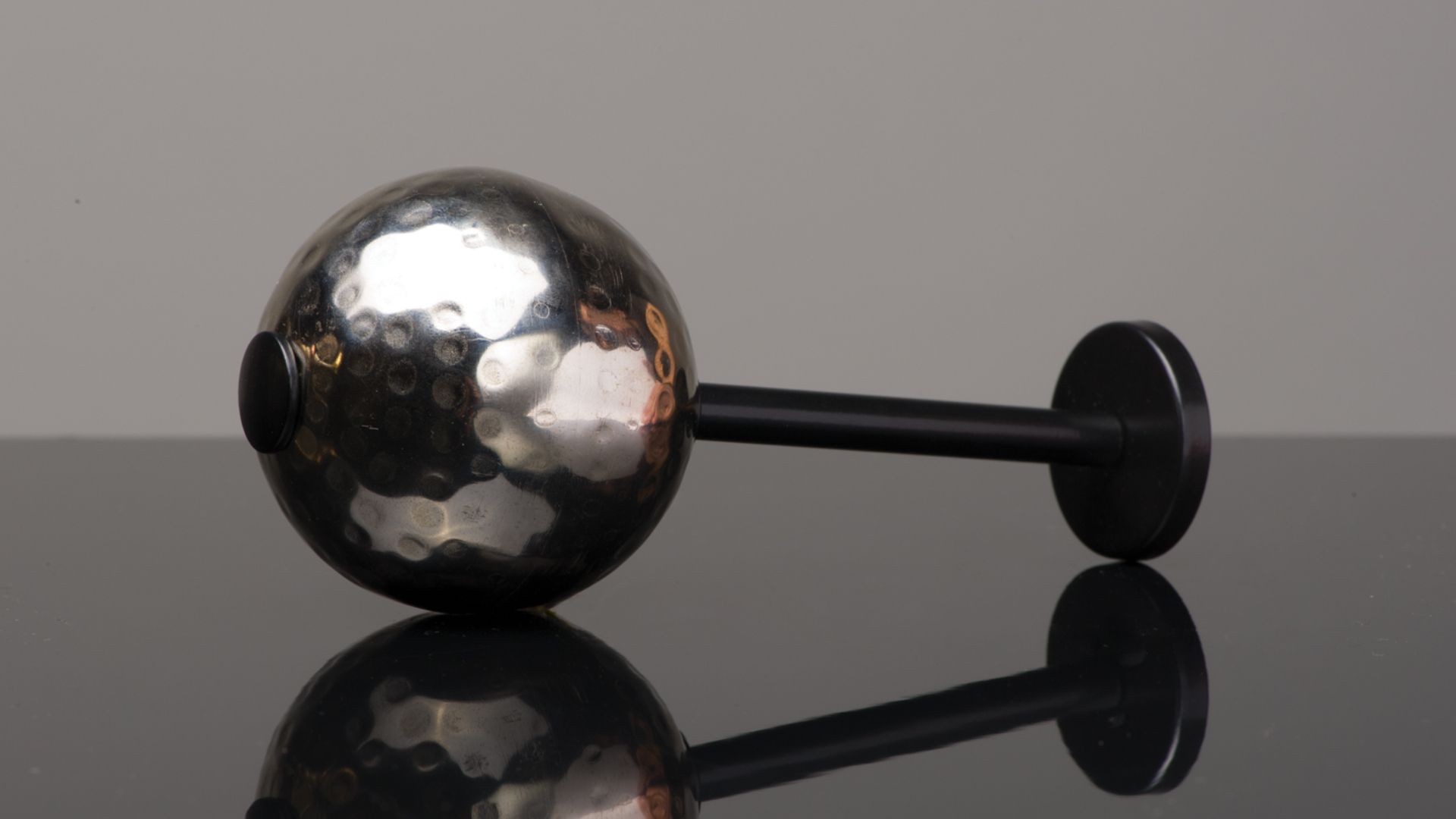 Chrome and black toy dumbbell on a reflective black surface