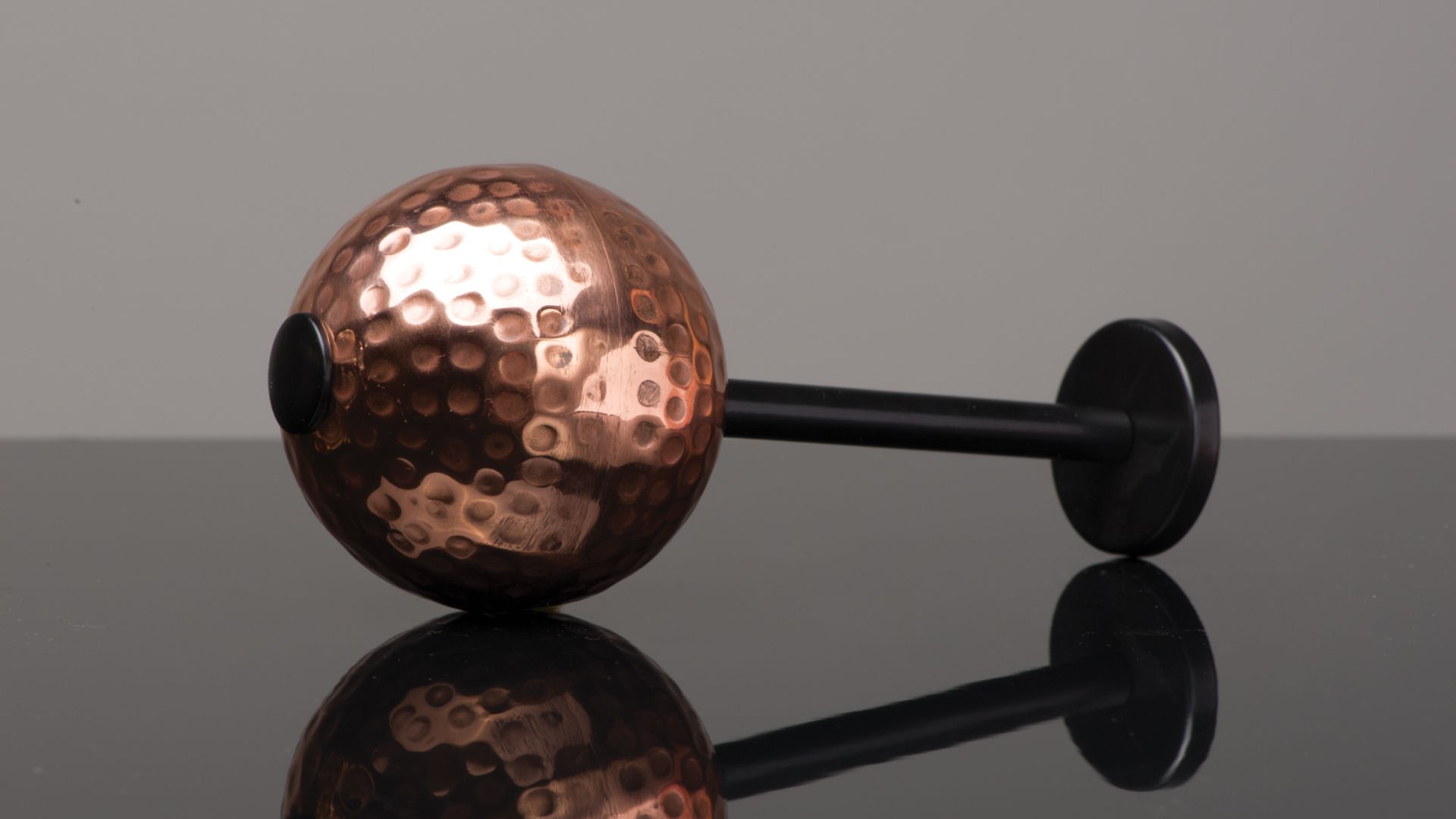 Copper hammered sphere with black handle on a reflective surface