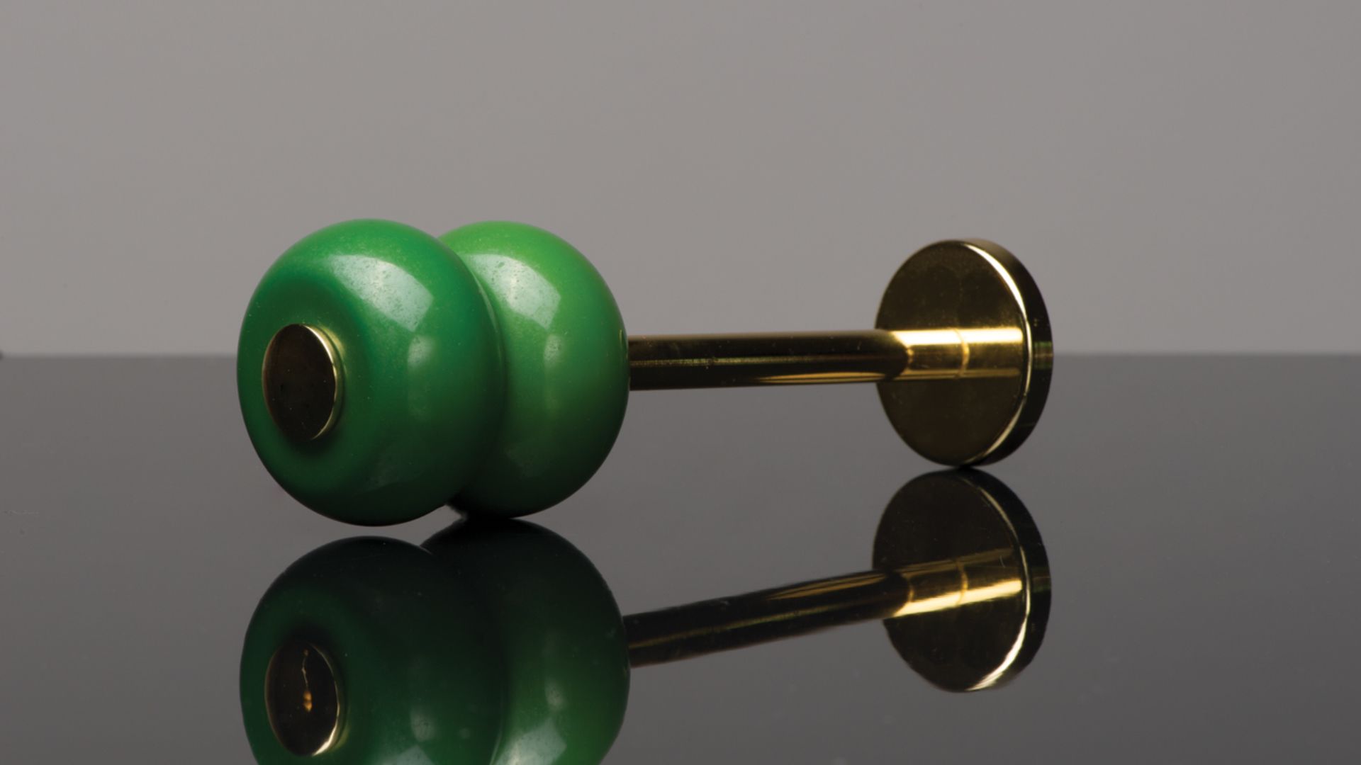 Green and gold dumbbell-shaped object on a reflective surface, shown in side view.