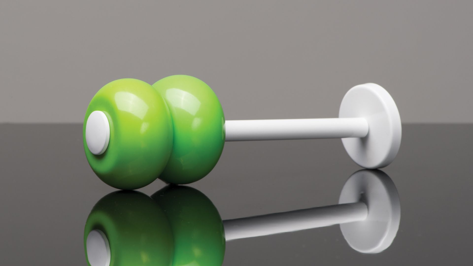 Two green dumbbells with white handles on a reflective surface