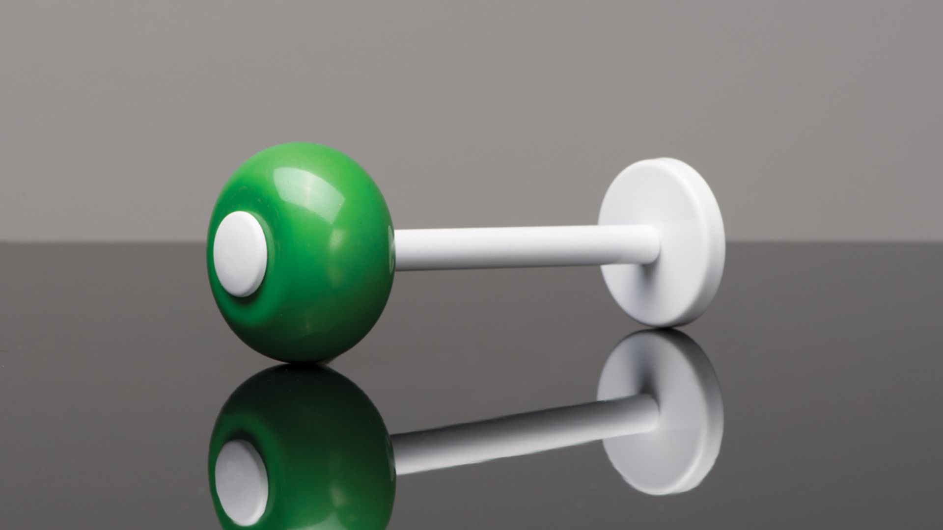 Green and white pushpin lying on a reflective surface