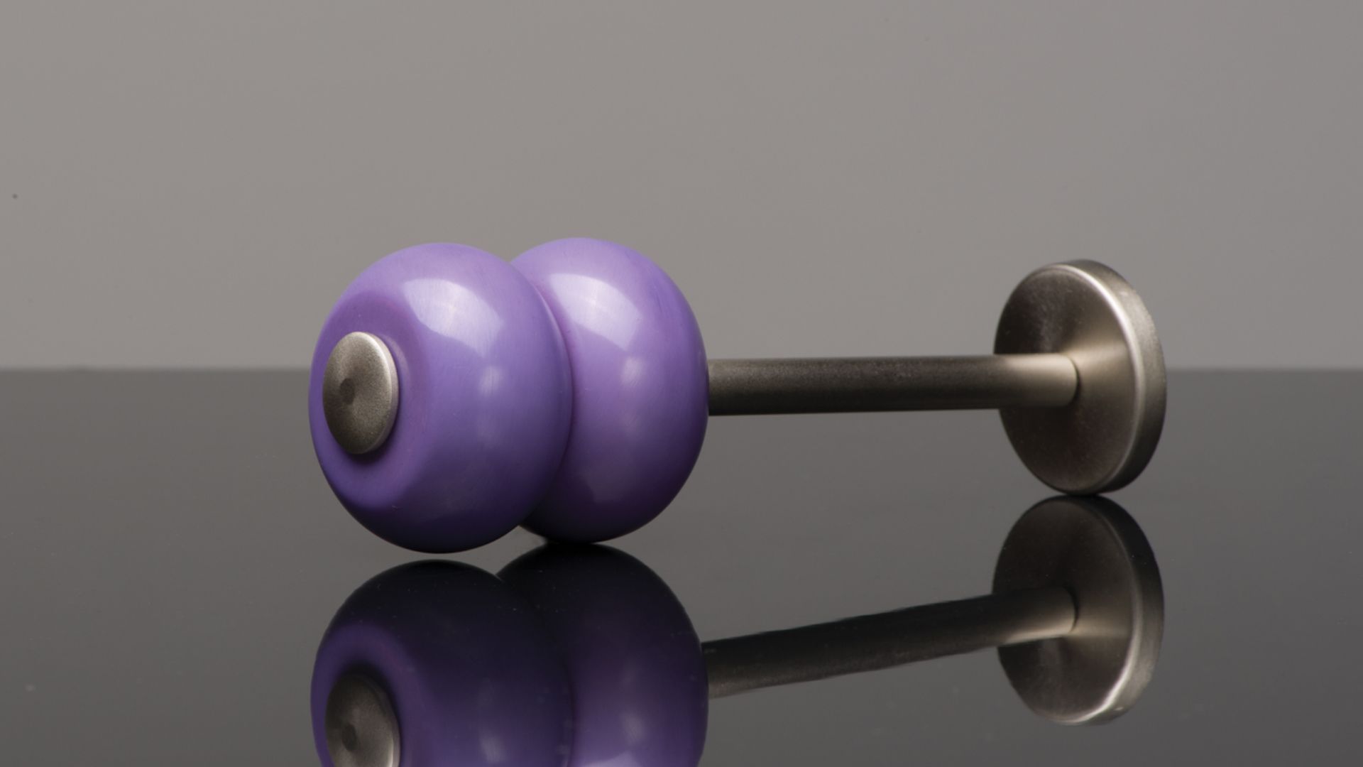 Purple dumbbell with black handle and silver end, resting on a glossy black surface with reflection.