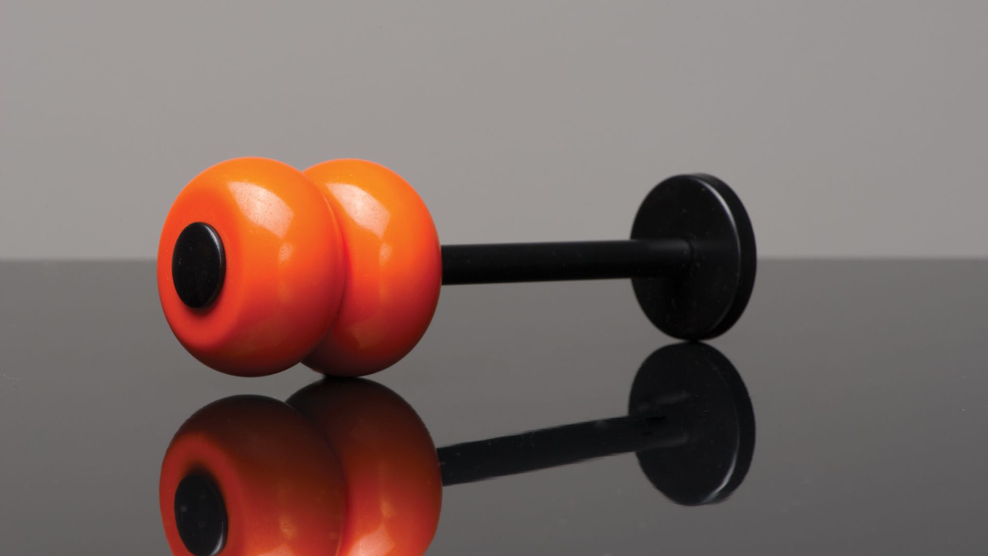 Two orange dumbbells on a glossy surface, with black handles and a mirrored reflection.