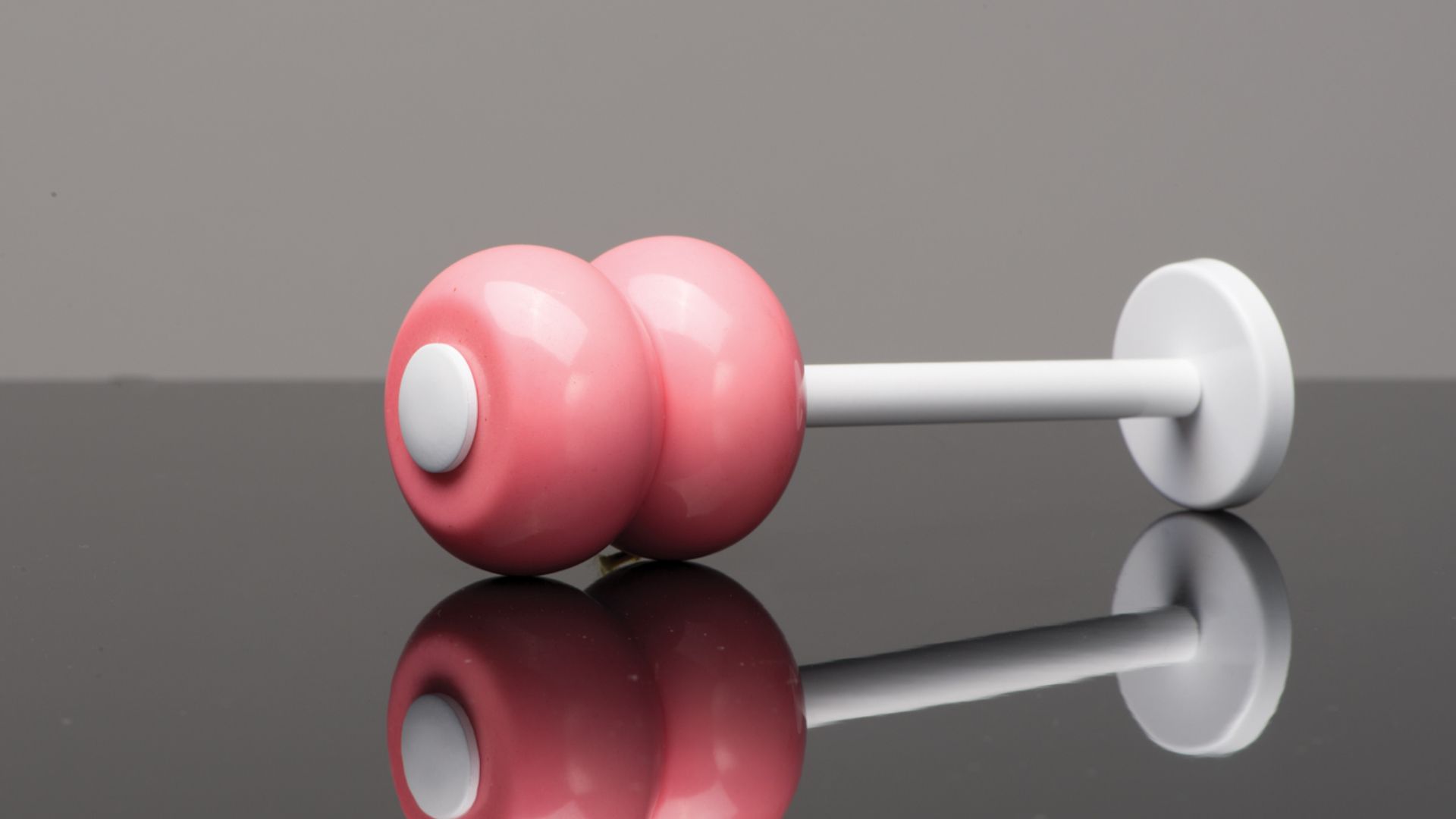 Pink dumbbell resting on a glossy reflective surface against a gray background
