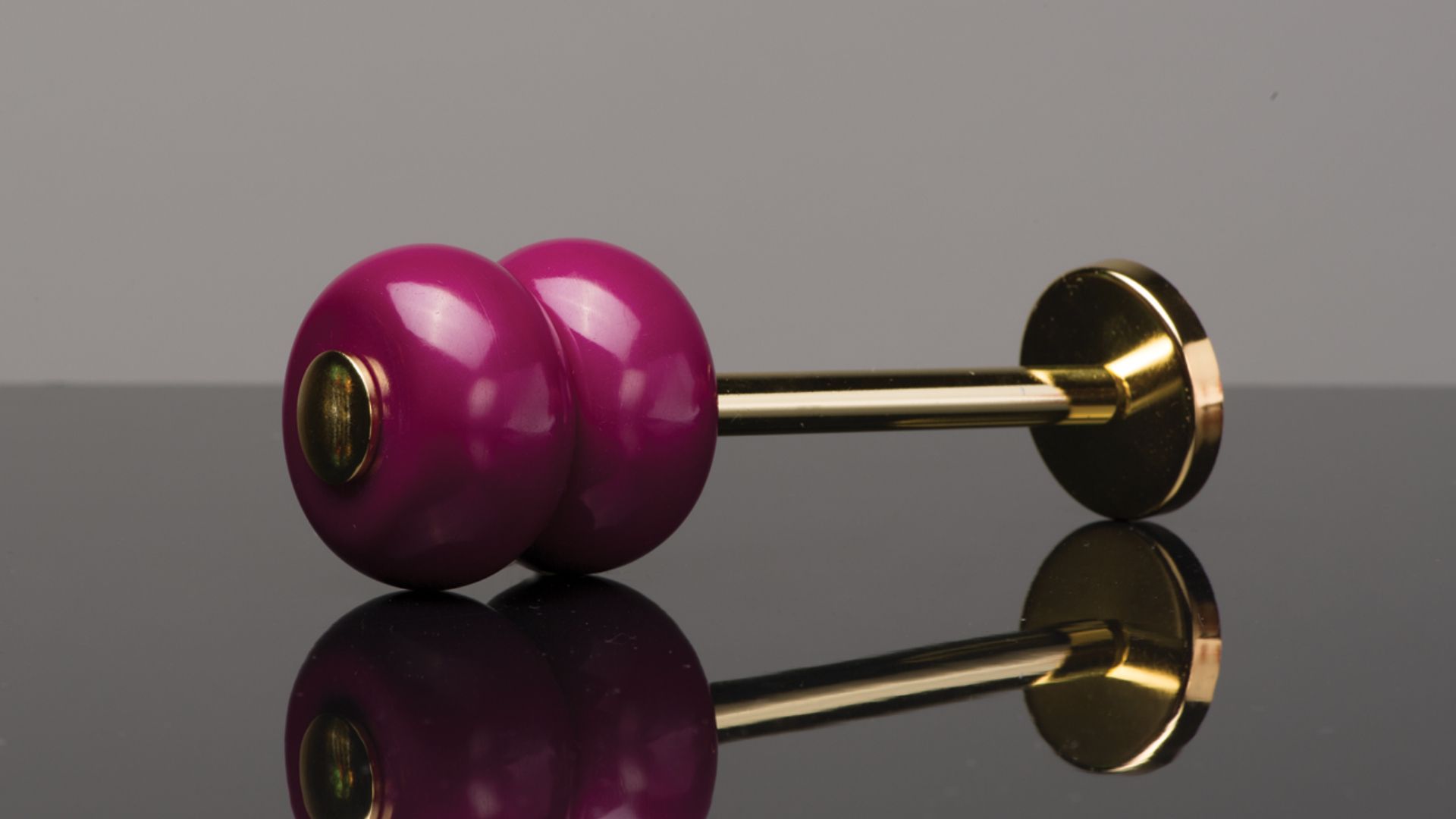 Purple dumbbell with gold handle on a reflective black surface