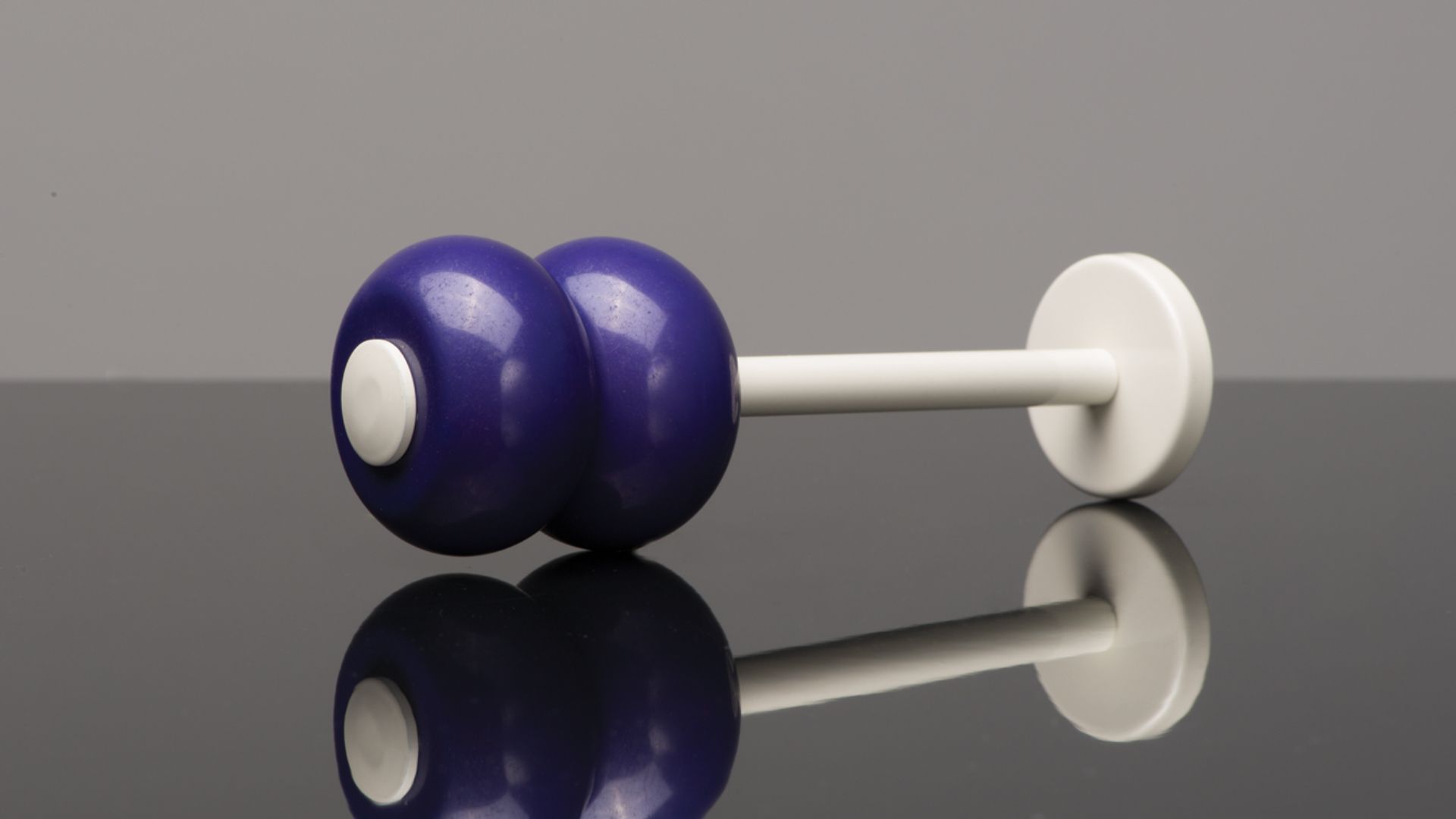 Purple dumbbell with white handle resting on a reflective surface