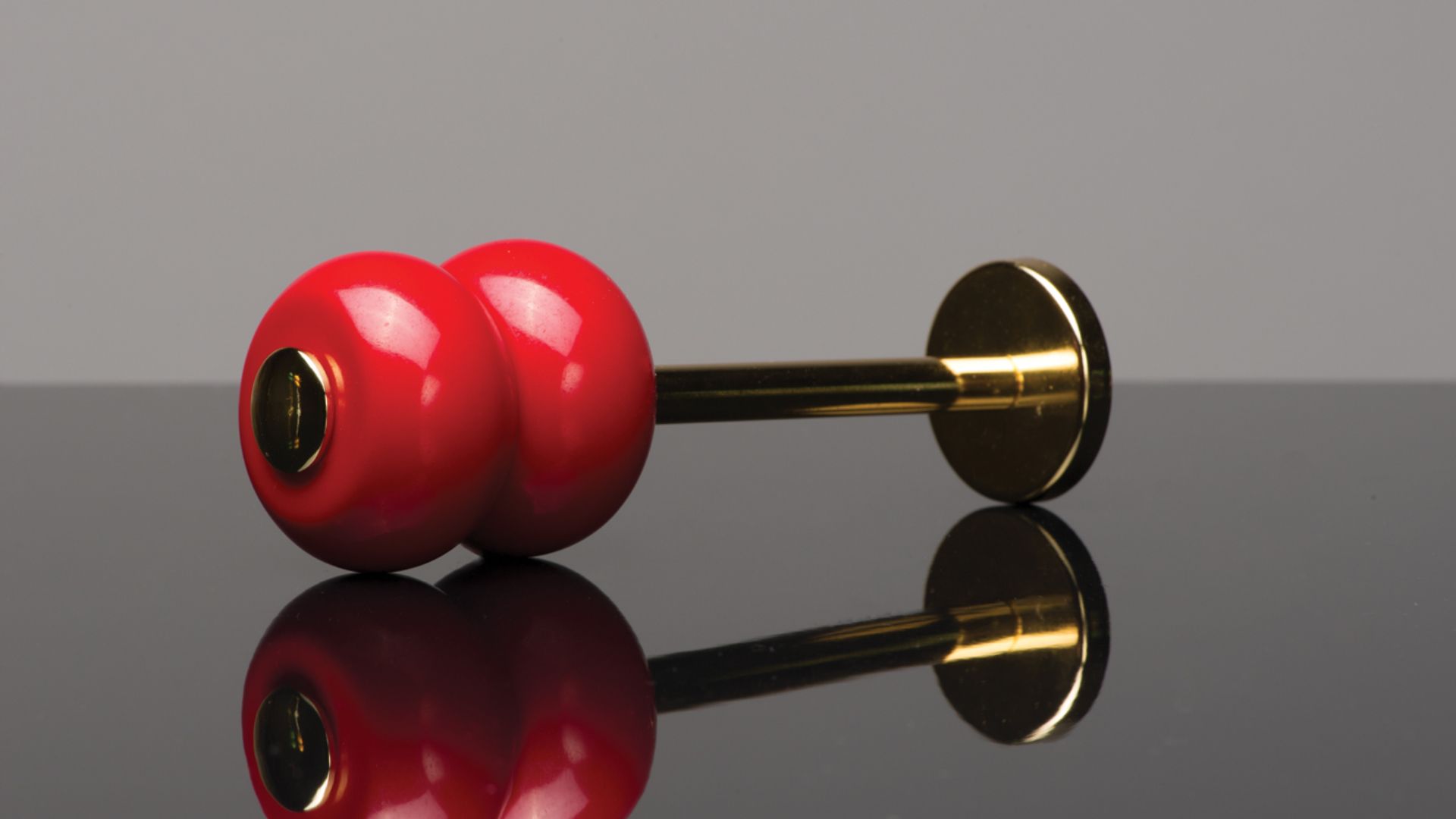 Red earplugs with a gold stem resting on a reflective gray surface.