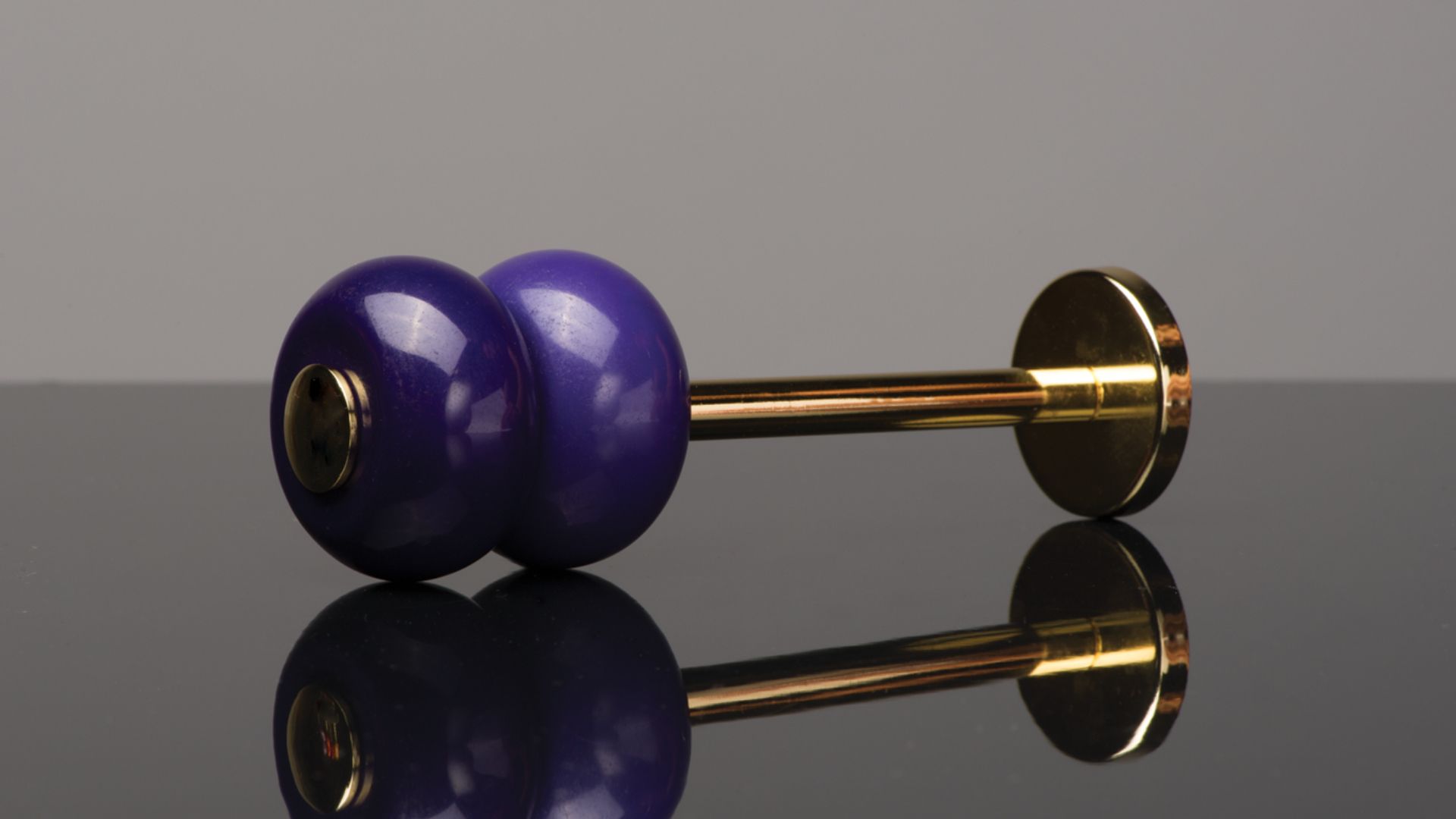 Purple dumbbell with gold handles resting on a reflective black surface.