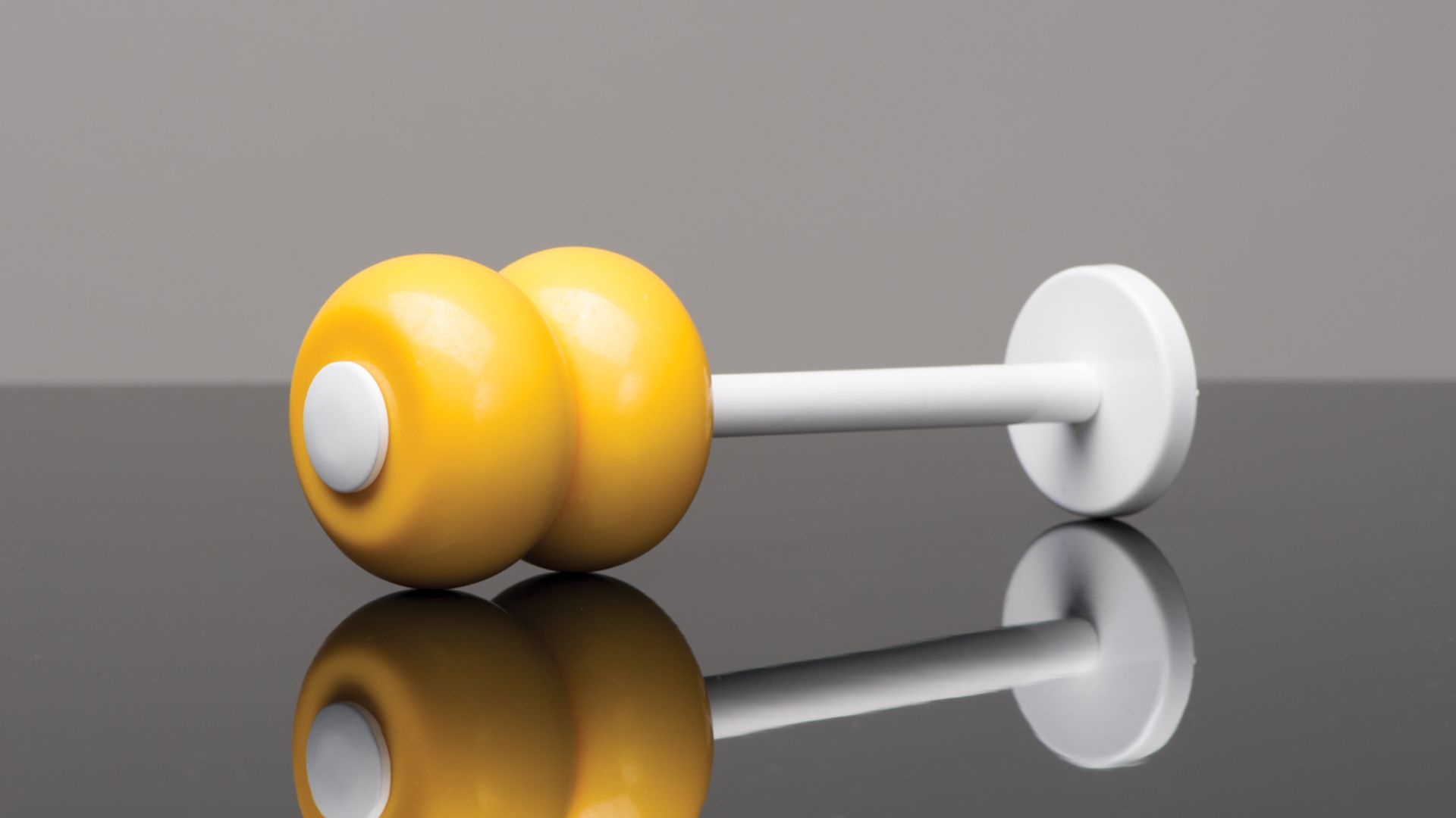 Yellow dumbbell on a reflective gray surface with a white handle and mirrored reflection