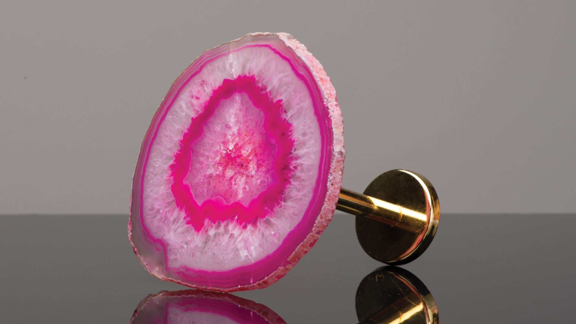 Pink and white sliced geode on a gold stand against a gray background