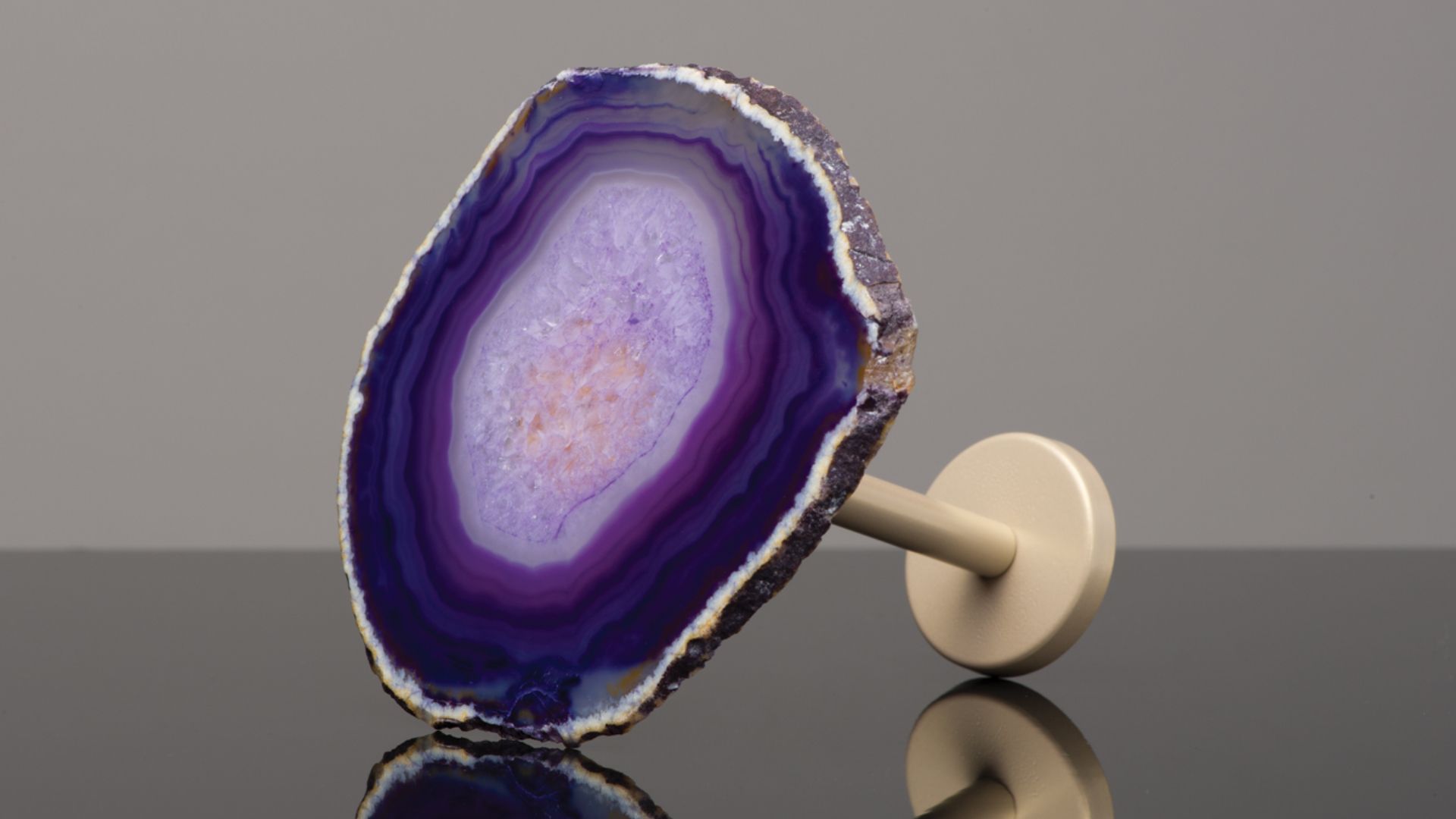 Purple geode slice on a small beige stand against a gray background