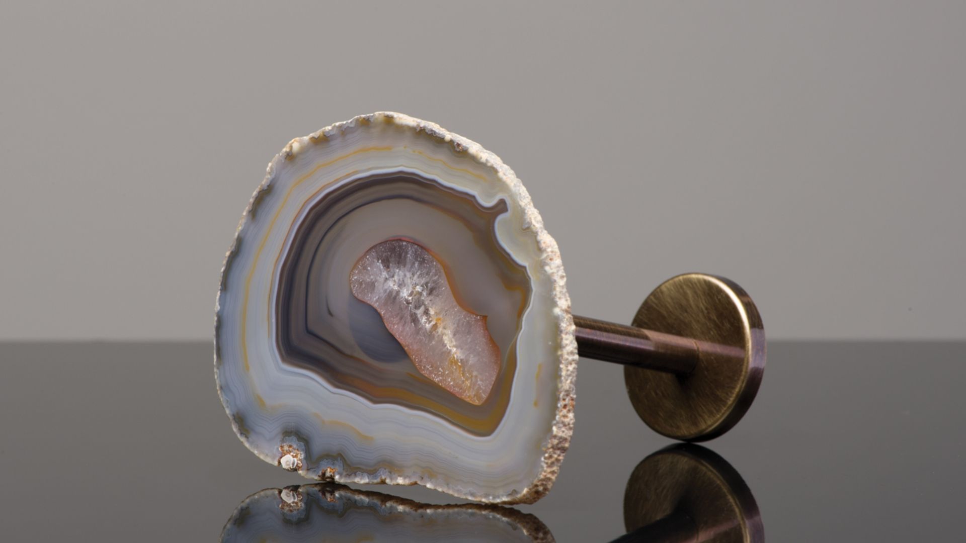 Polished agate slice with gold-tone stand on a reflective surface