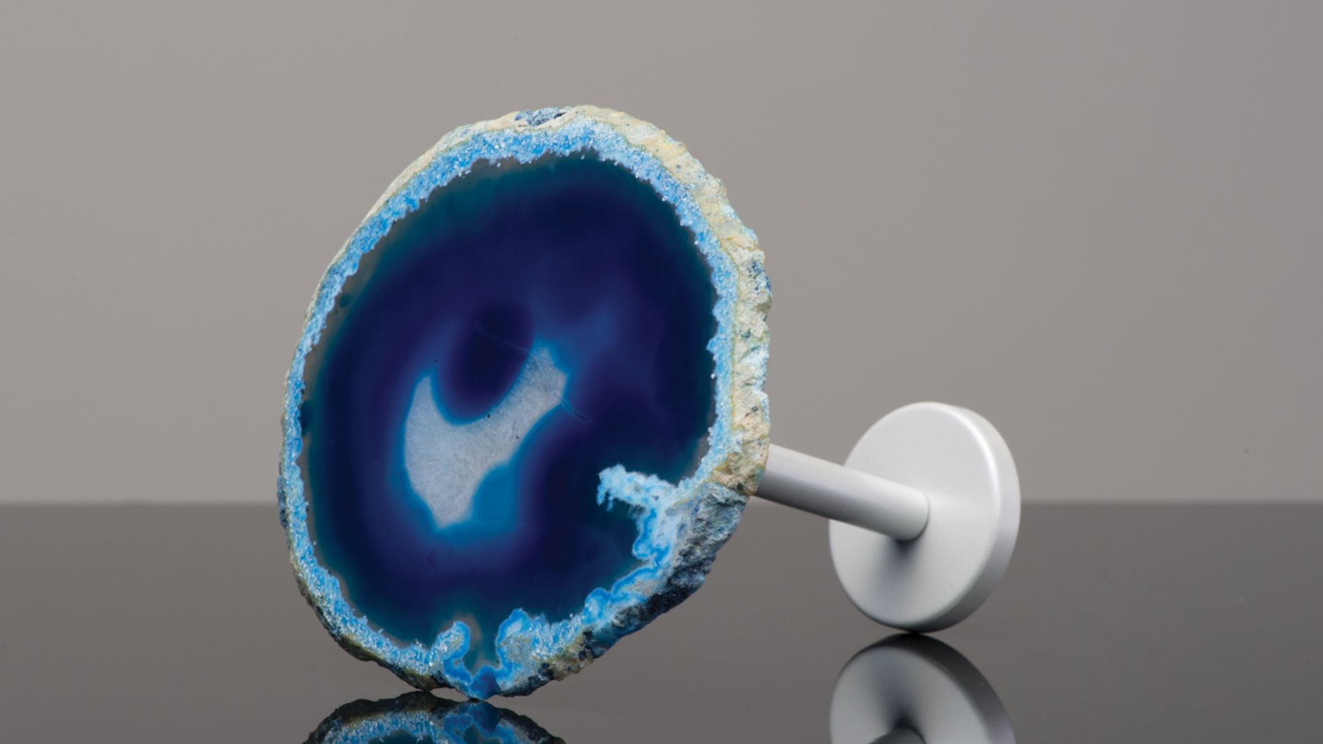 Blue and white circular glass ornament on a white stand against a gray background