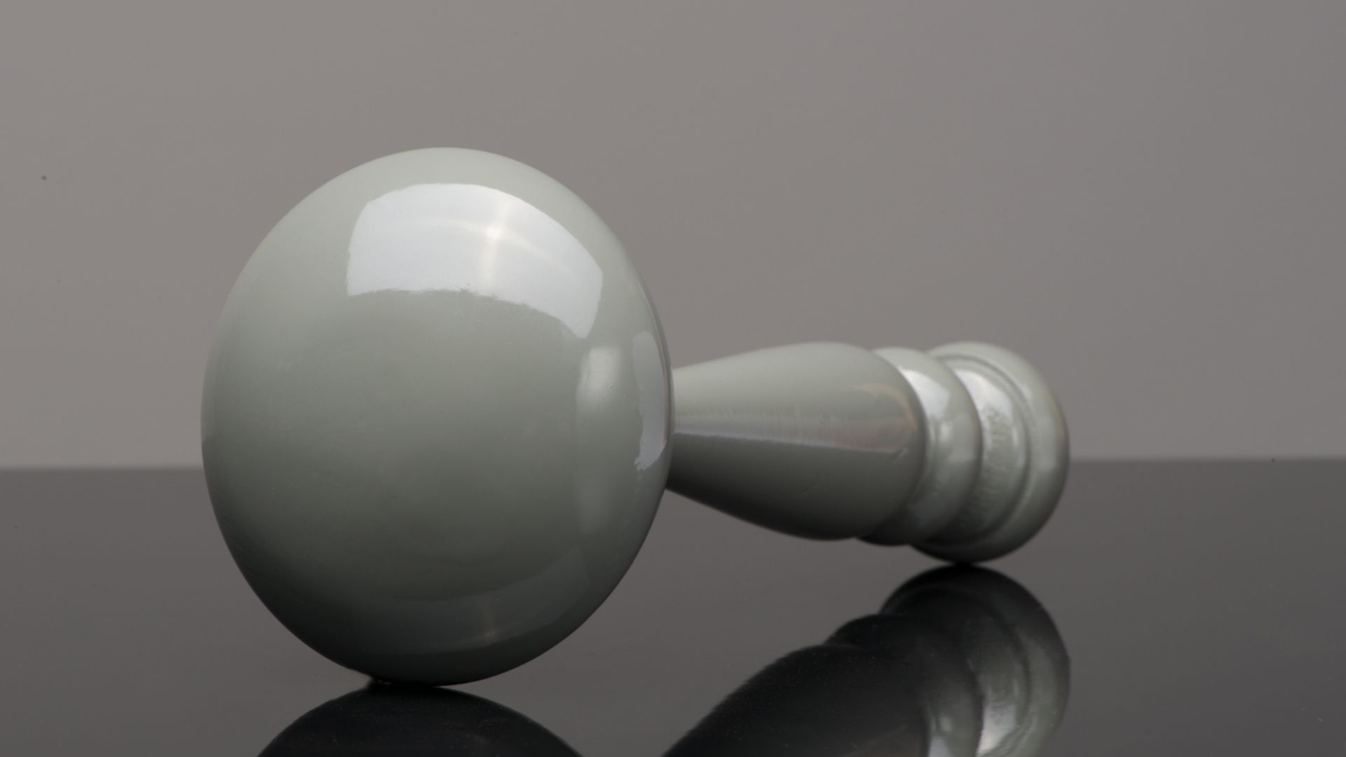 White pawn-like game piece lying on its side on a reflective gray surface.
