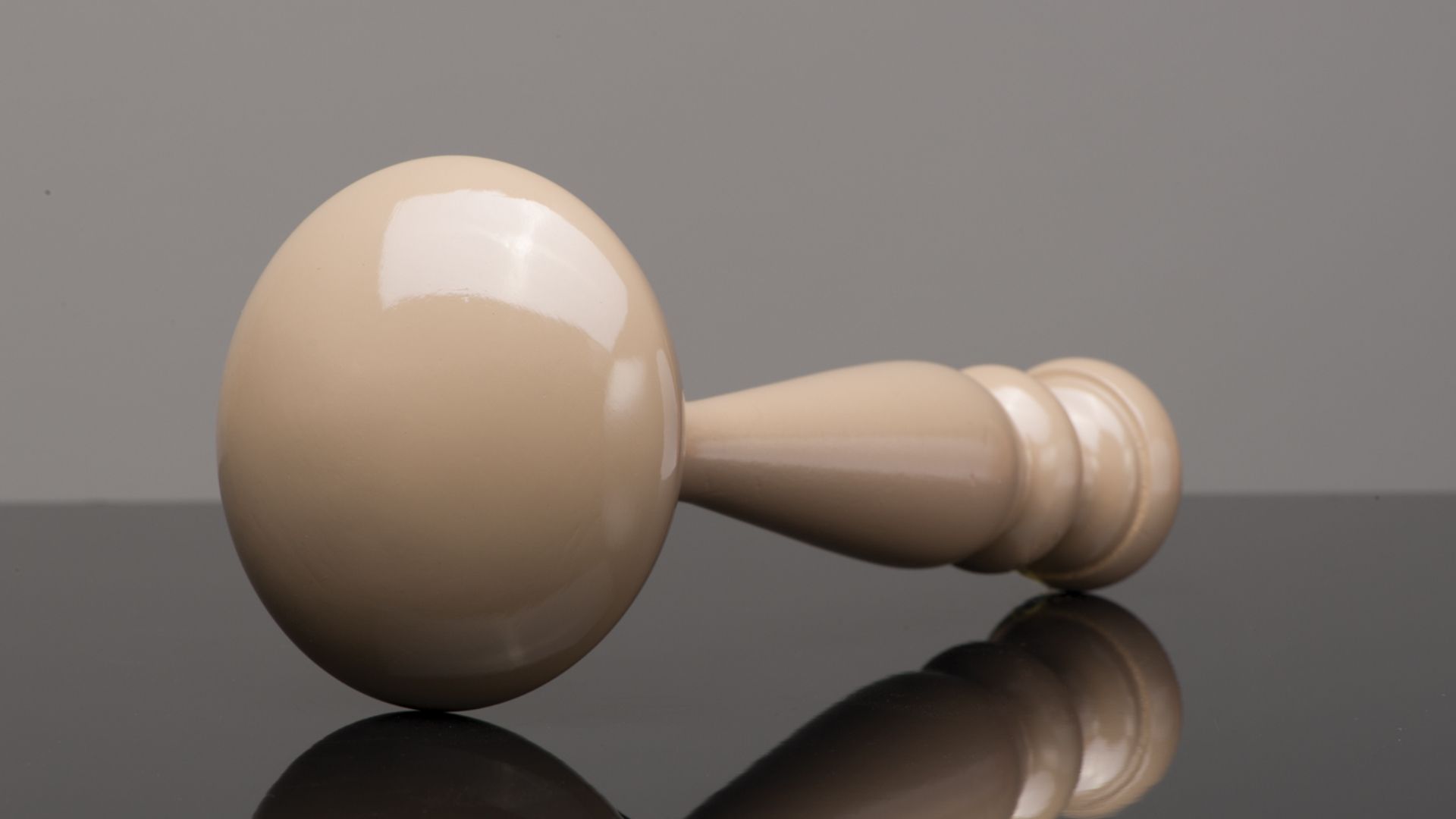 Wooden massage roller with a rounded head on a reflective surface, against a gray background