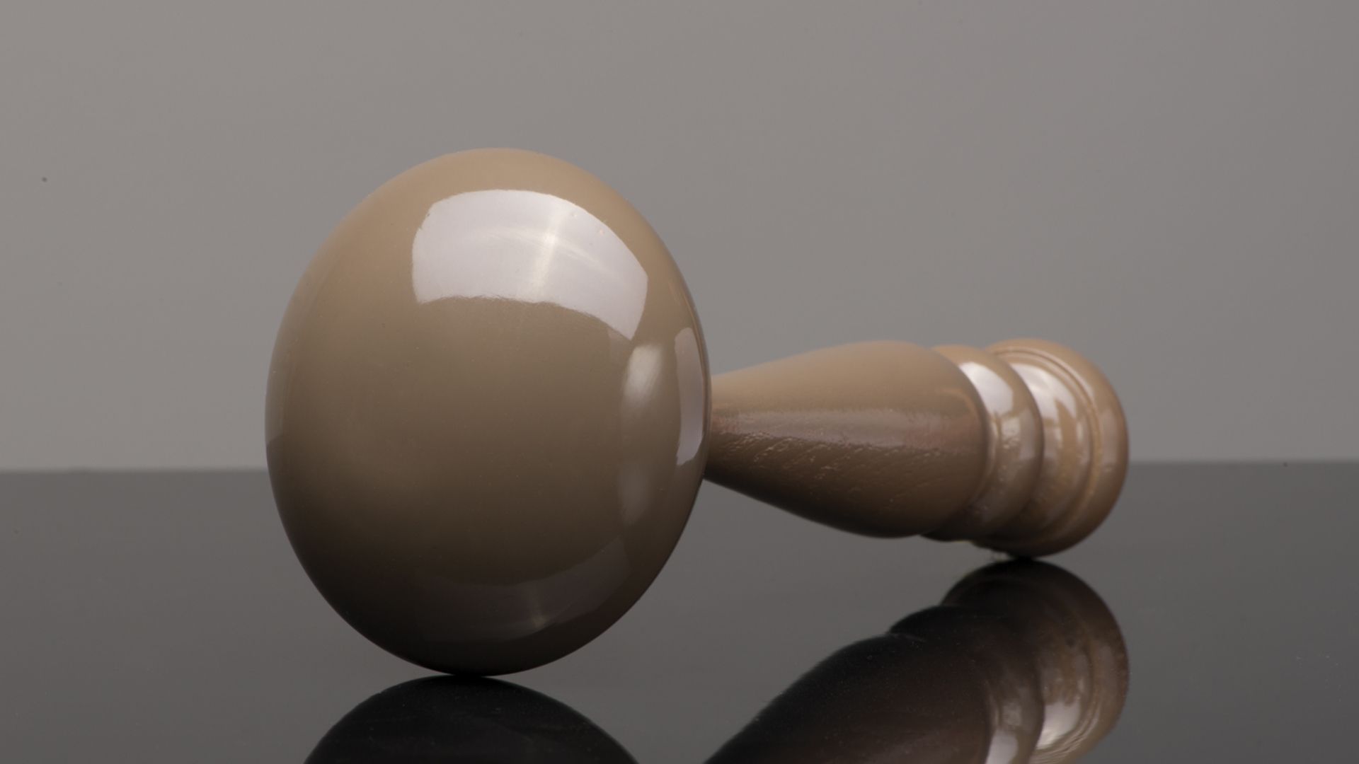 Wooden gavel lying on a reflective surface, shown in close-up against a gray background.
