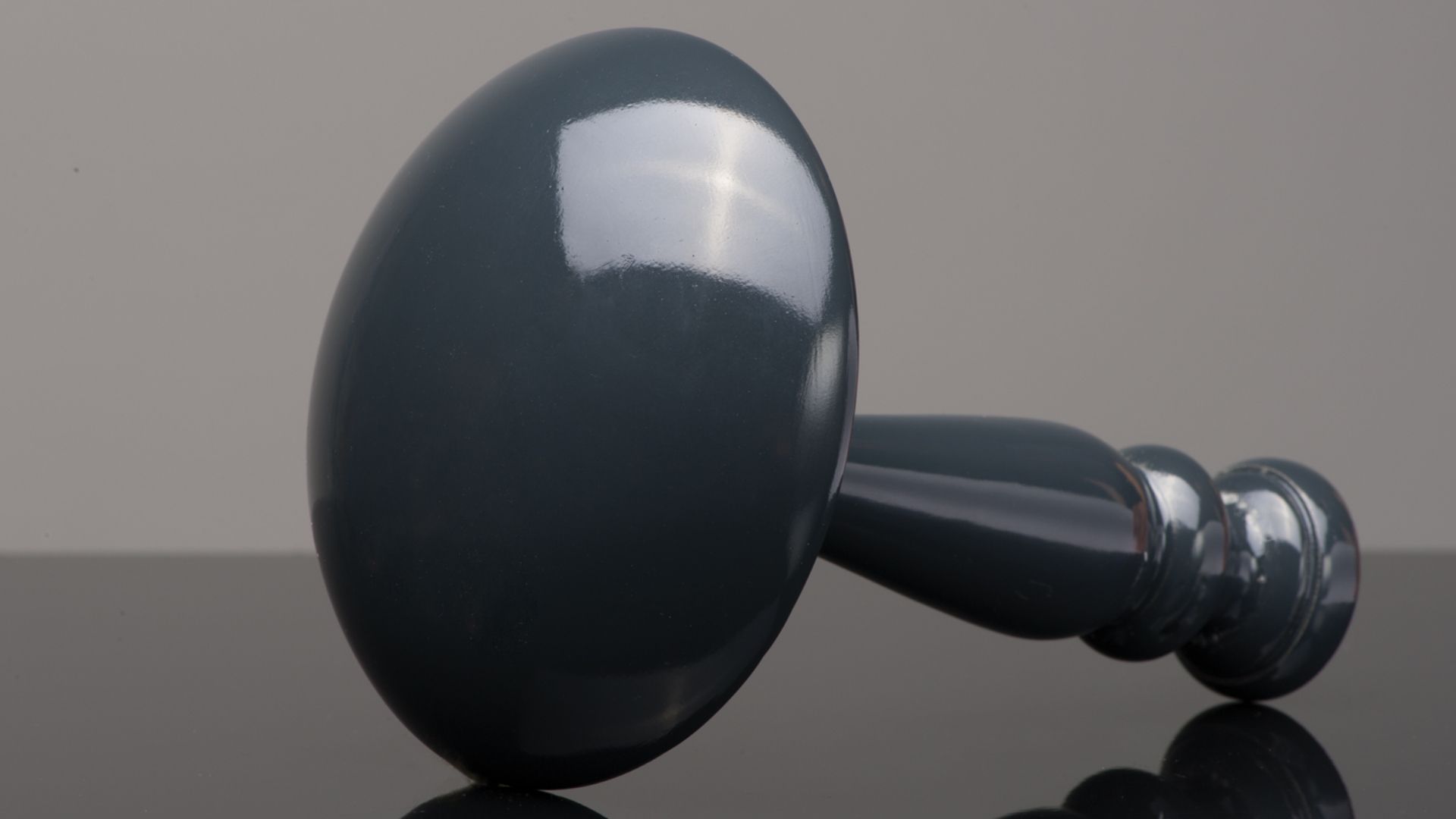 Black glossy bowling pin lying on its side on a reflective gray surface