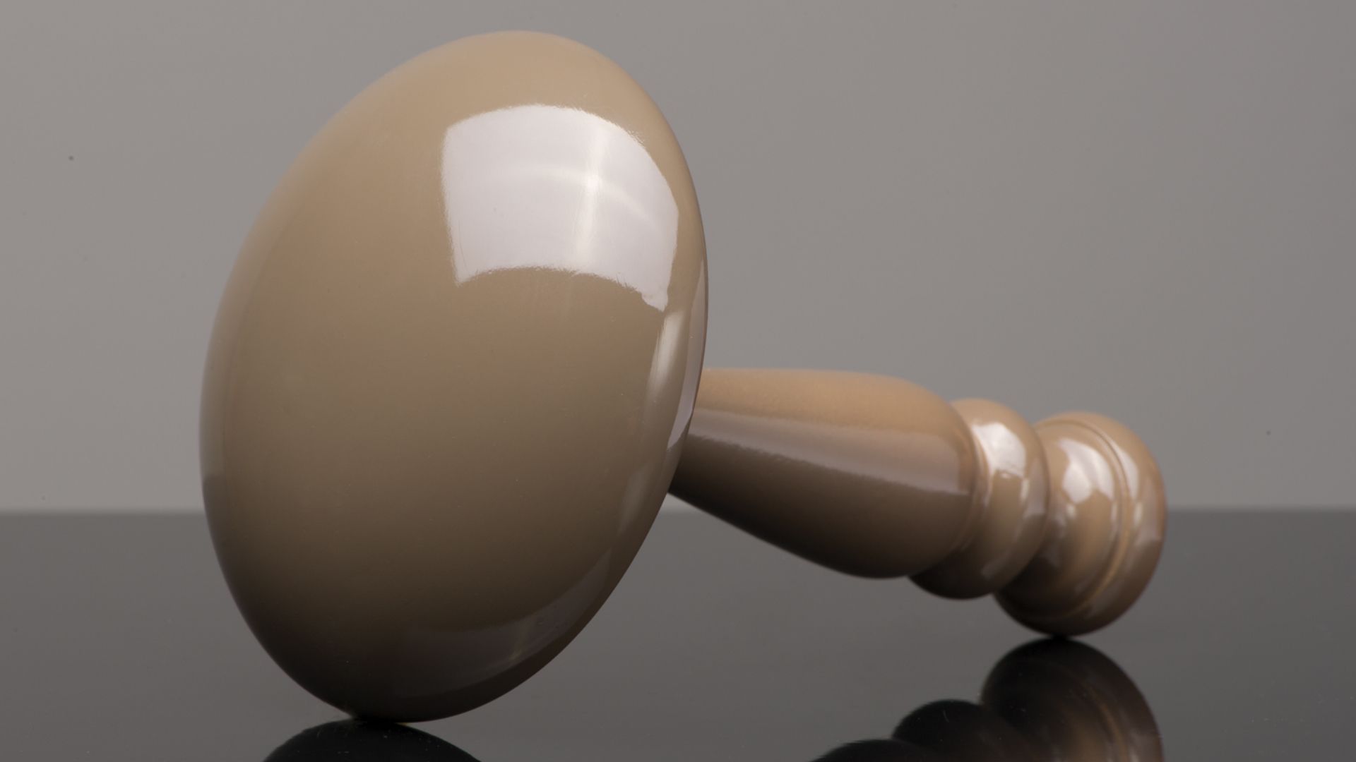 Wooden gavel lying on its side on a reflective surface against a gray background