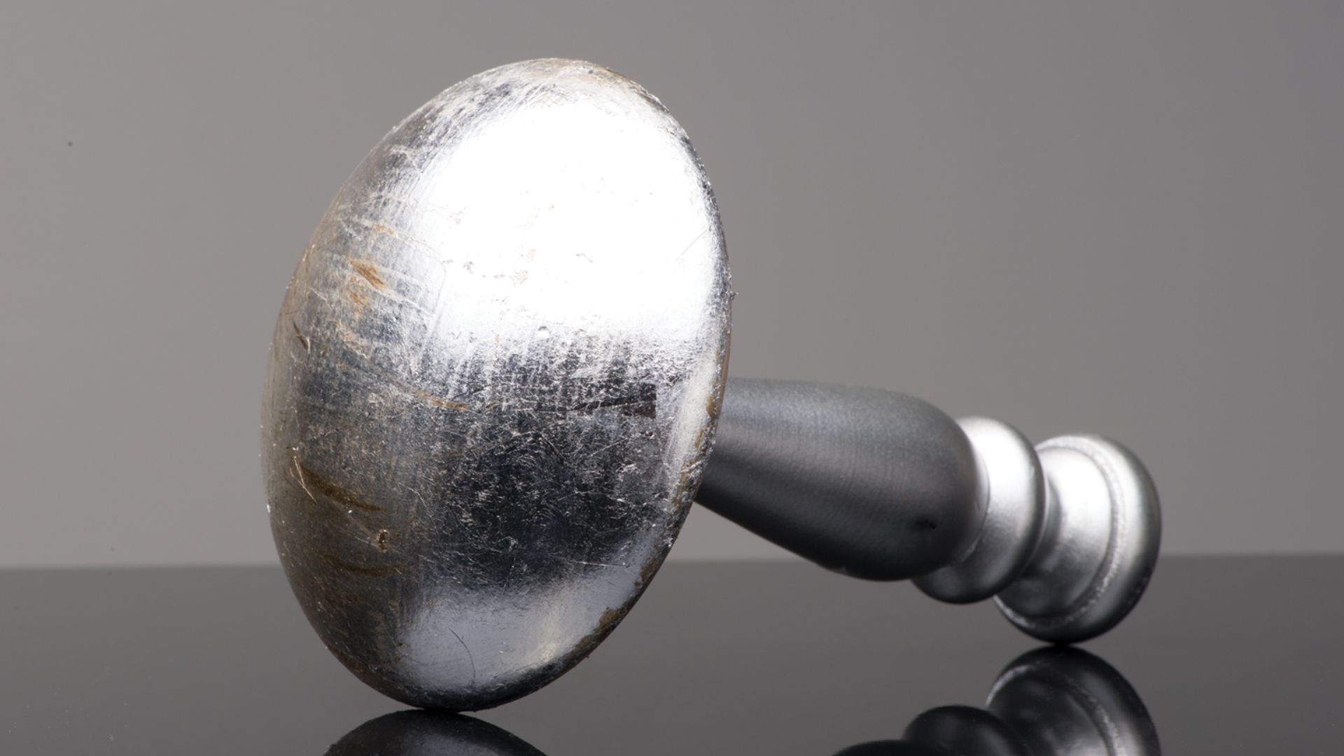 Silver hammer lying on a reflective black surface against a gray background