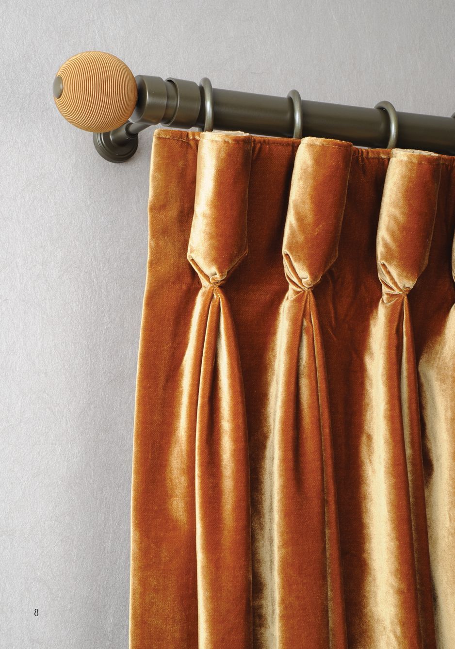 Copper curtains on a black rod with a decorative finial against a light gray wall