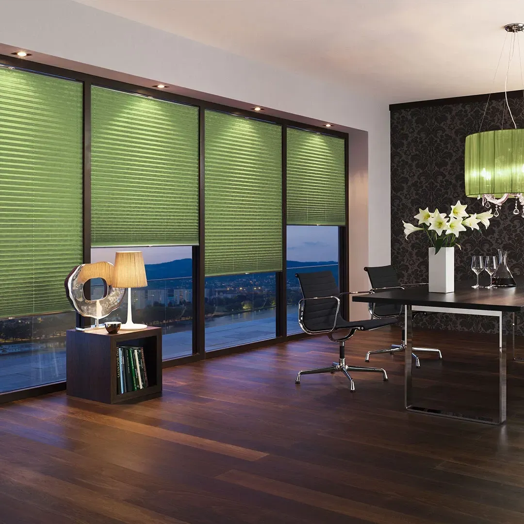 Modern living room with green blinds, dark wood floors, and a dining table by large windows overlooking water.