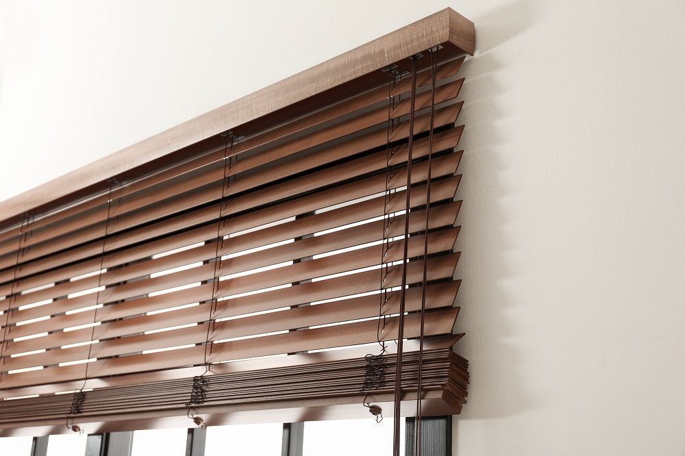 Brown wooden window blinds with a pull cord against a white wall